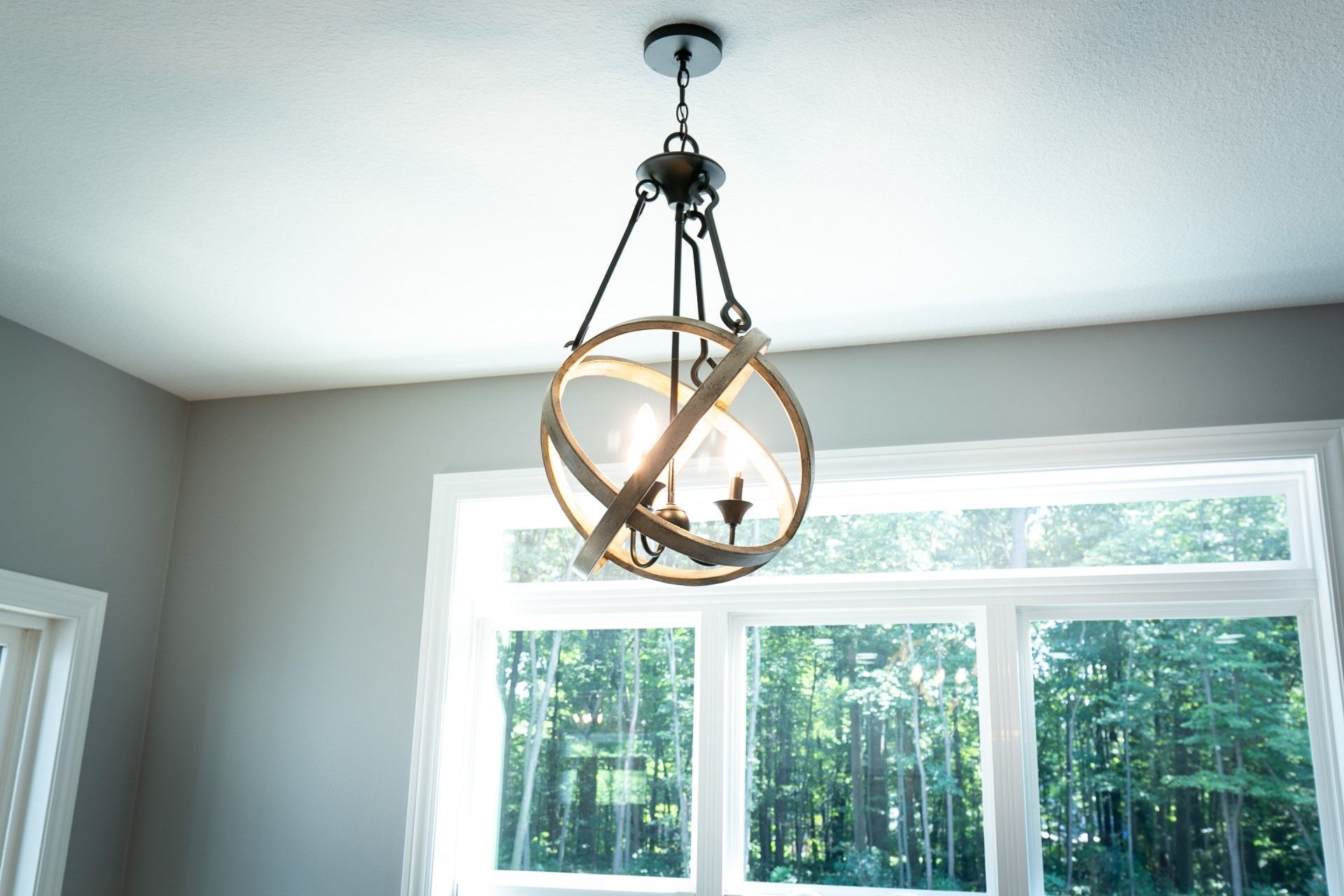 Orb-shaped chandelier hanging from a white ceiling, above a large window. Daylight shines through the window.