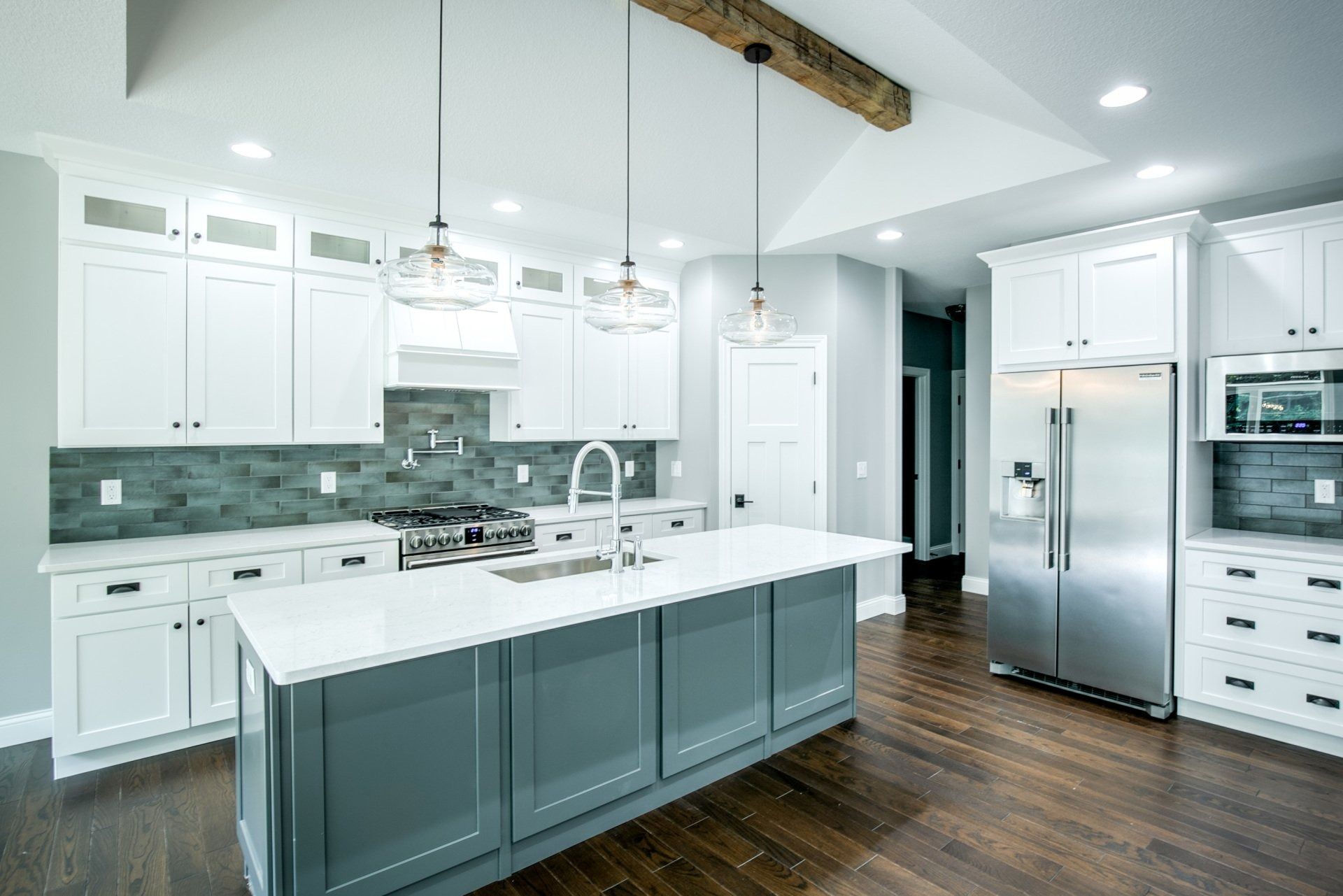 Modern kitchen with white cabinets, gray island, stainless steel appliances, and dark wood floors.