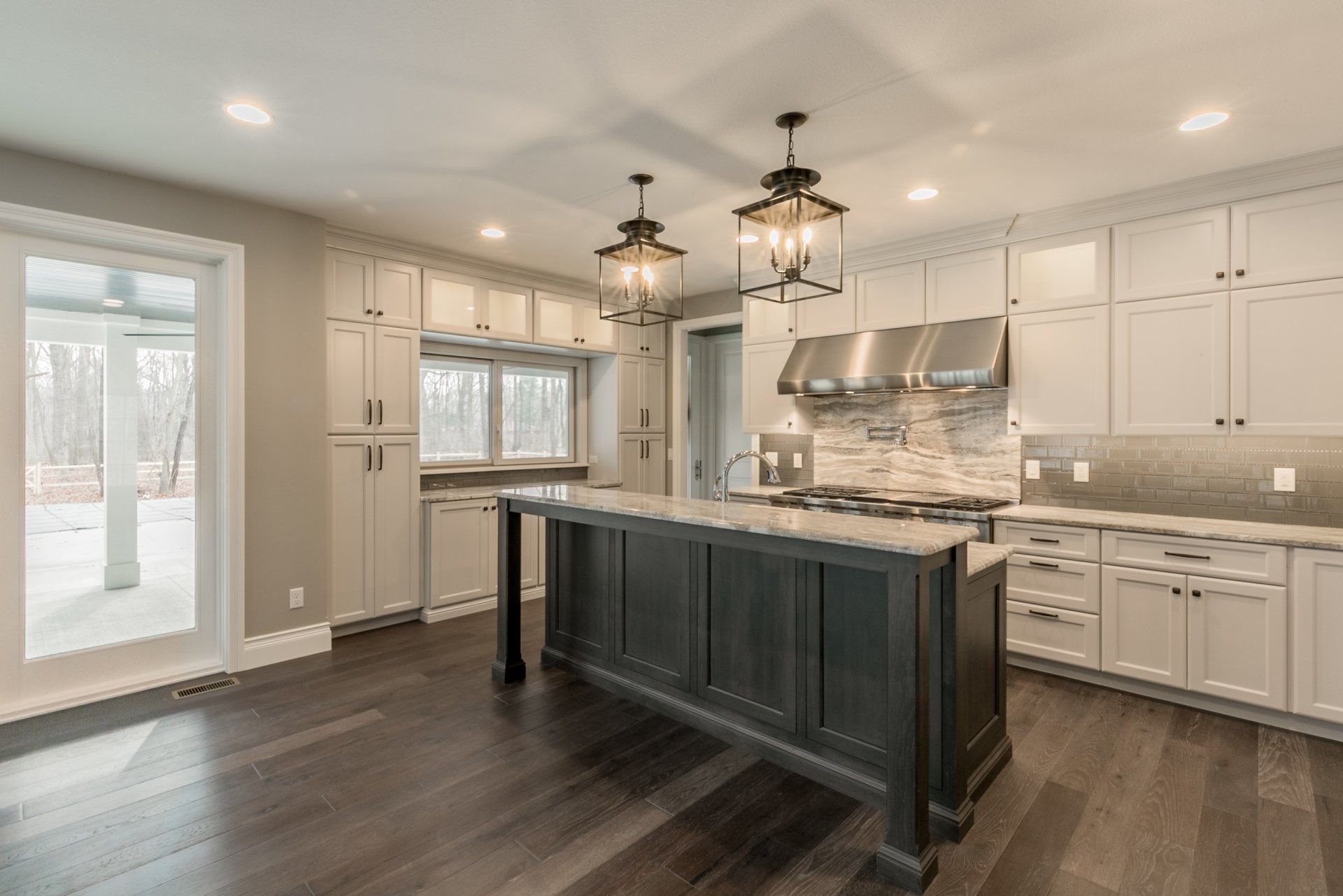 Modern kitchen with dark hardwood floors, white cabinets, and a gray island with two pendant lights.