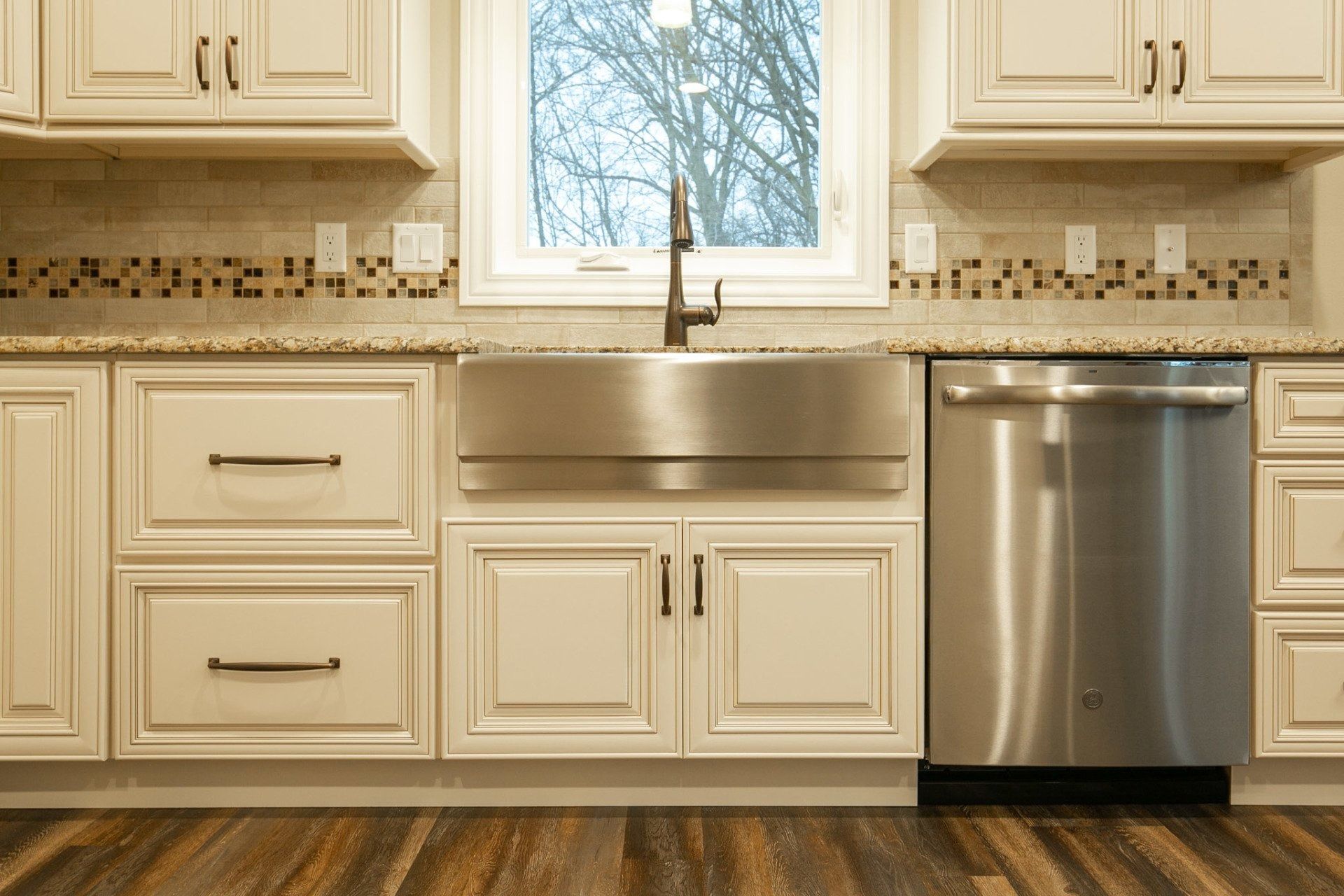 Kitchen with stainless steel sink and dishwasher, cream cabinets, and window.