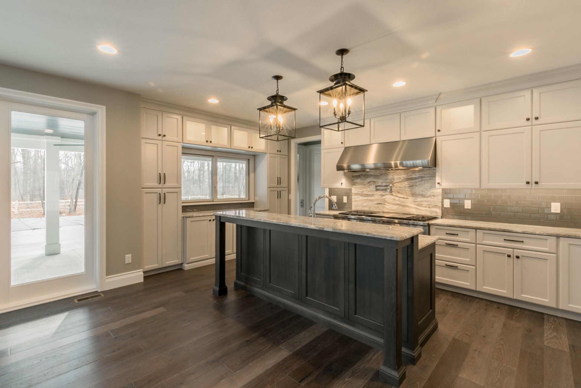 Modern kitchen with dark wood floors, white cabinets, and a gray island with two pendant lights.