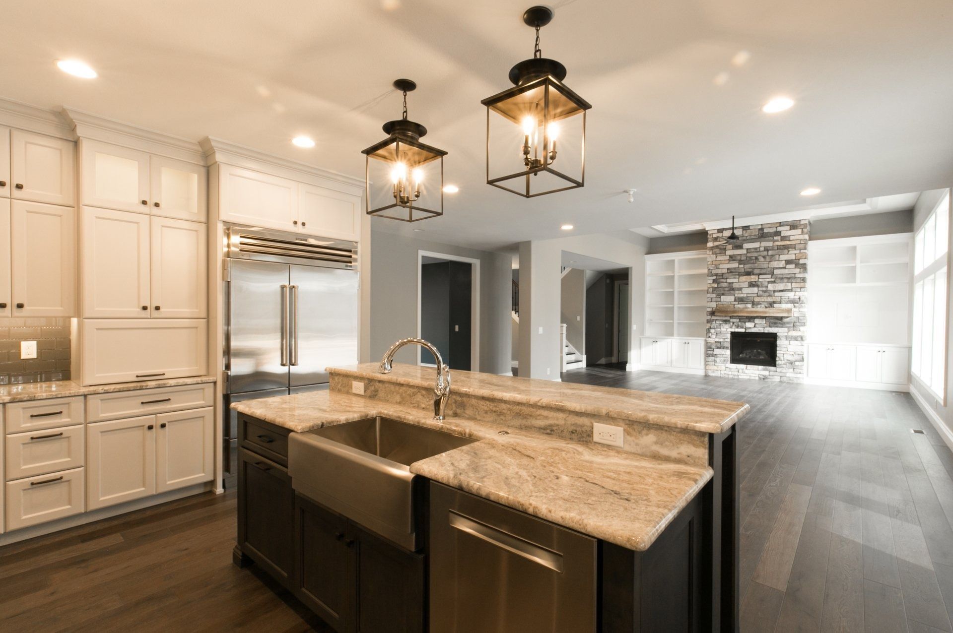 Modern kitchen with dark island, farmhouse sink, light granite counters, and lantern lights.