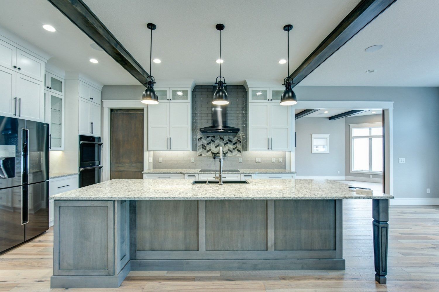 Modern kitchen with large island, granite countertop, pendant lights, and stainless steel appliances.