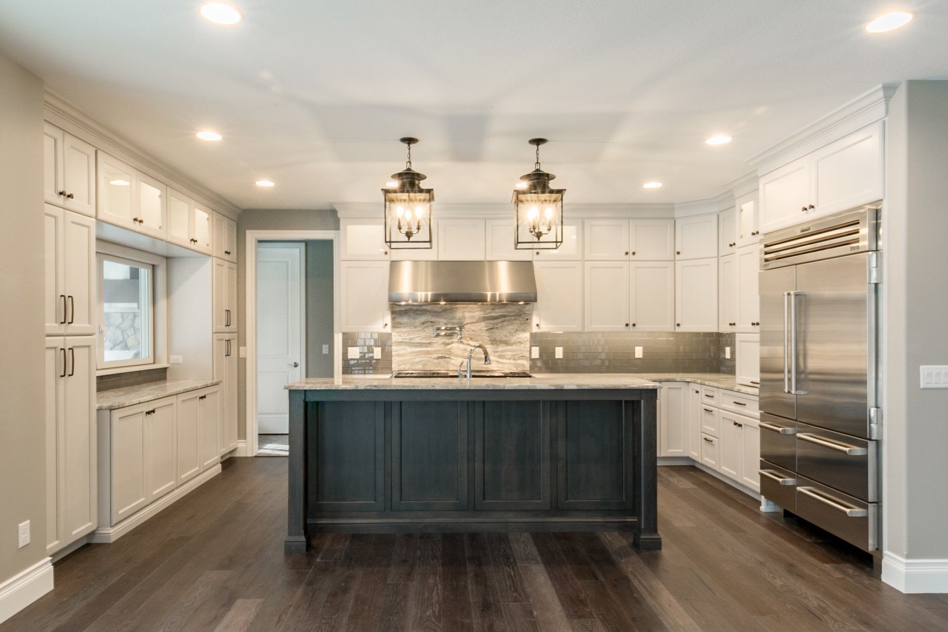 Modern kitchen with white cabinets, dark island, stainless steel appliances, and wood floors.
