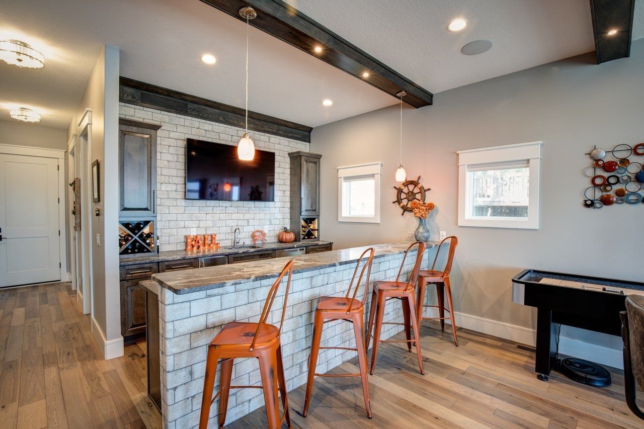 A home bar with brick-style facade, orange stools, and a TV; a doorway and game table are also in the room.