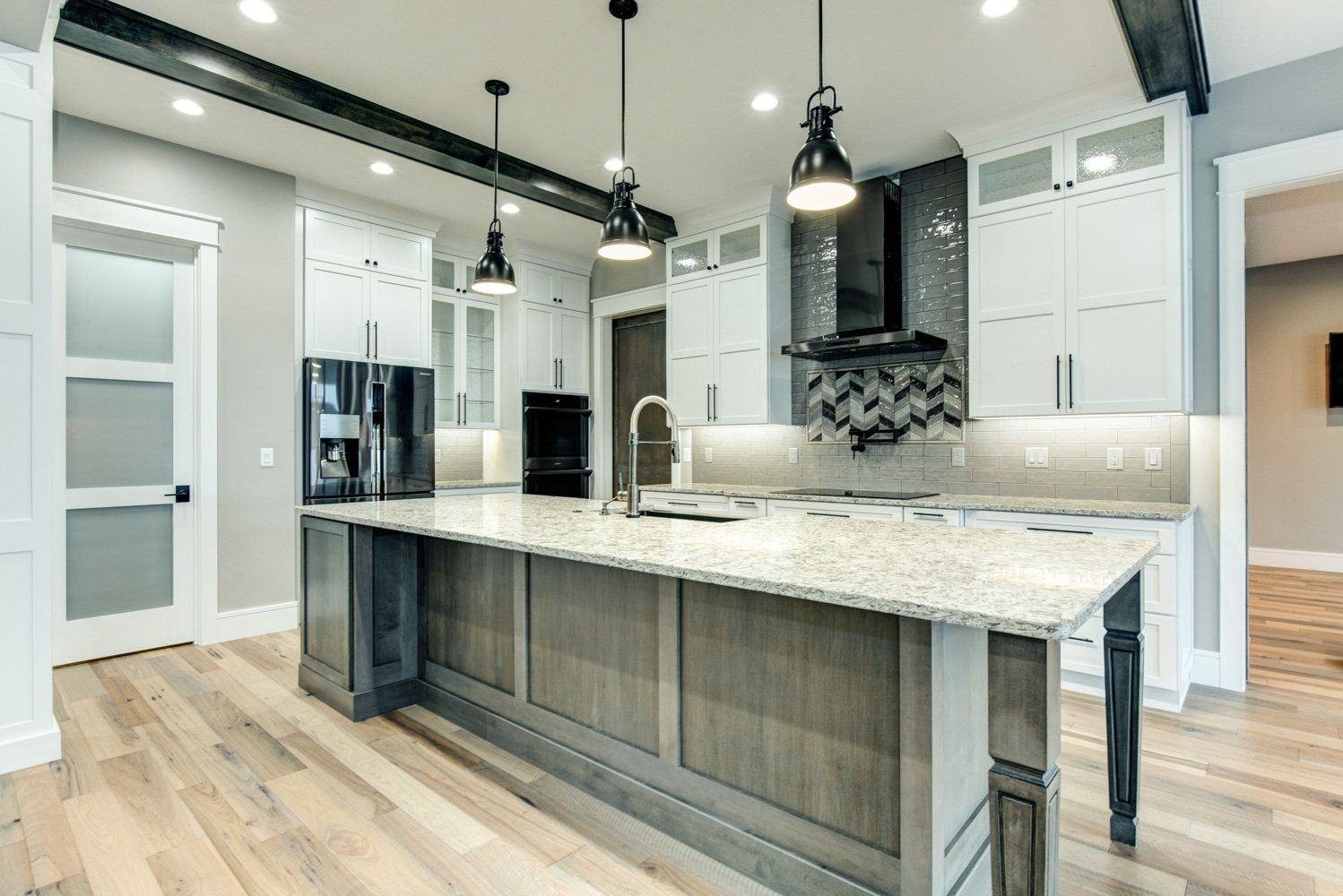 Modern kitchen with light wood floors, white cabinets, gray island, and black pendant lights.