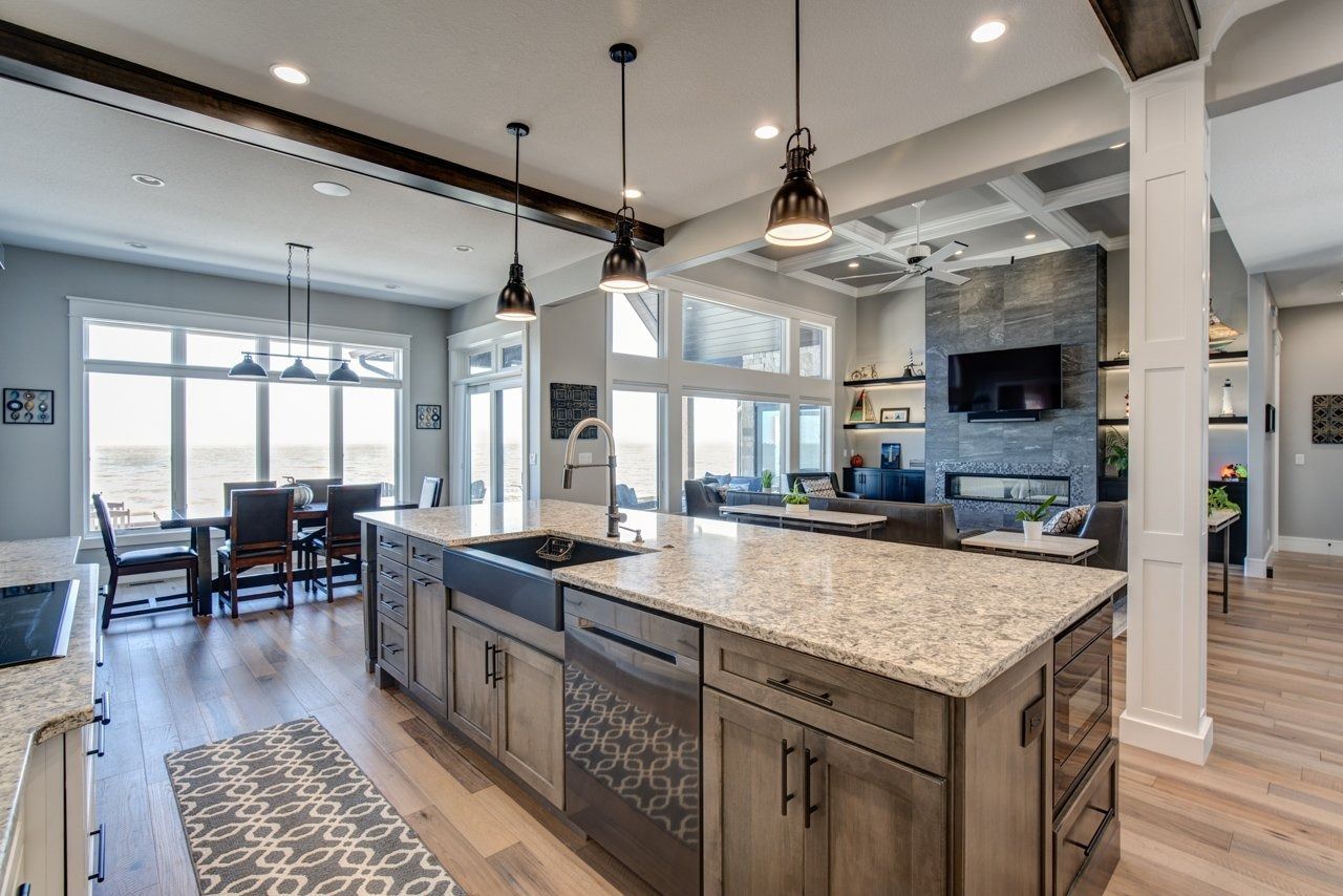 Open-concept kitchen with island, dining area, and living room; light wood floors and gray cabinets.