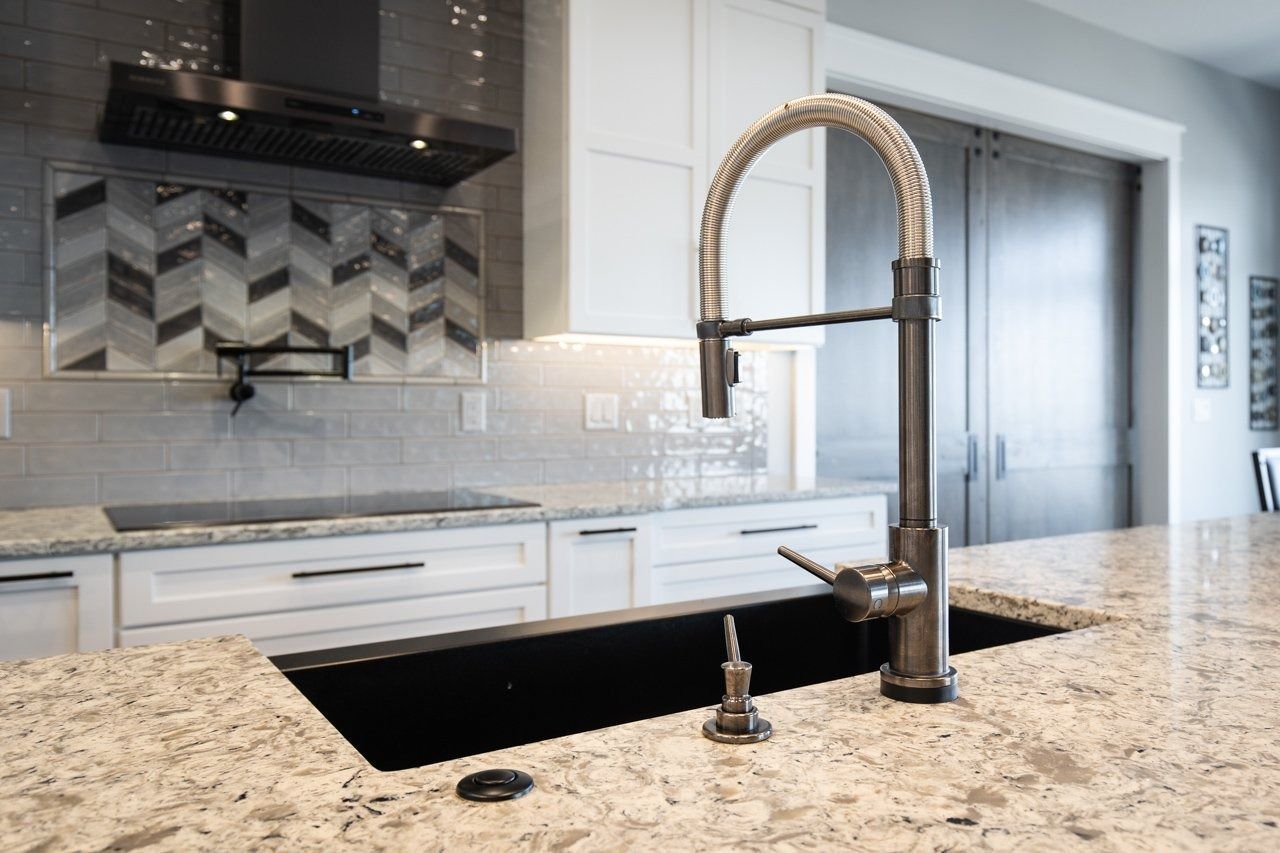 Kitchen with granite countertop, black sink, and a pull-down faucet. White cabinets, herringbone backsplash, and a black range hood.