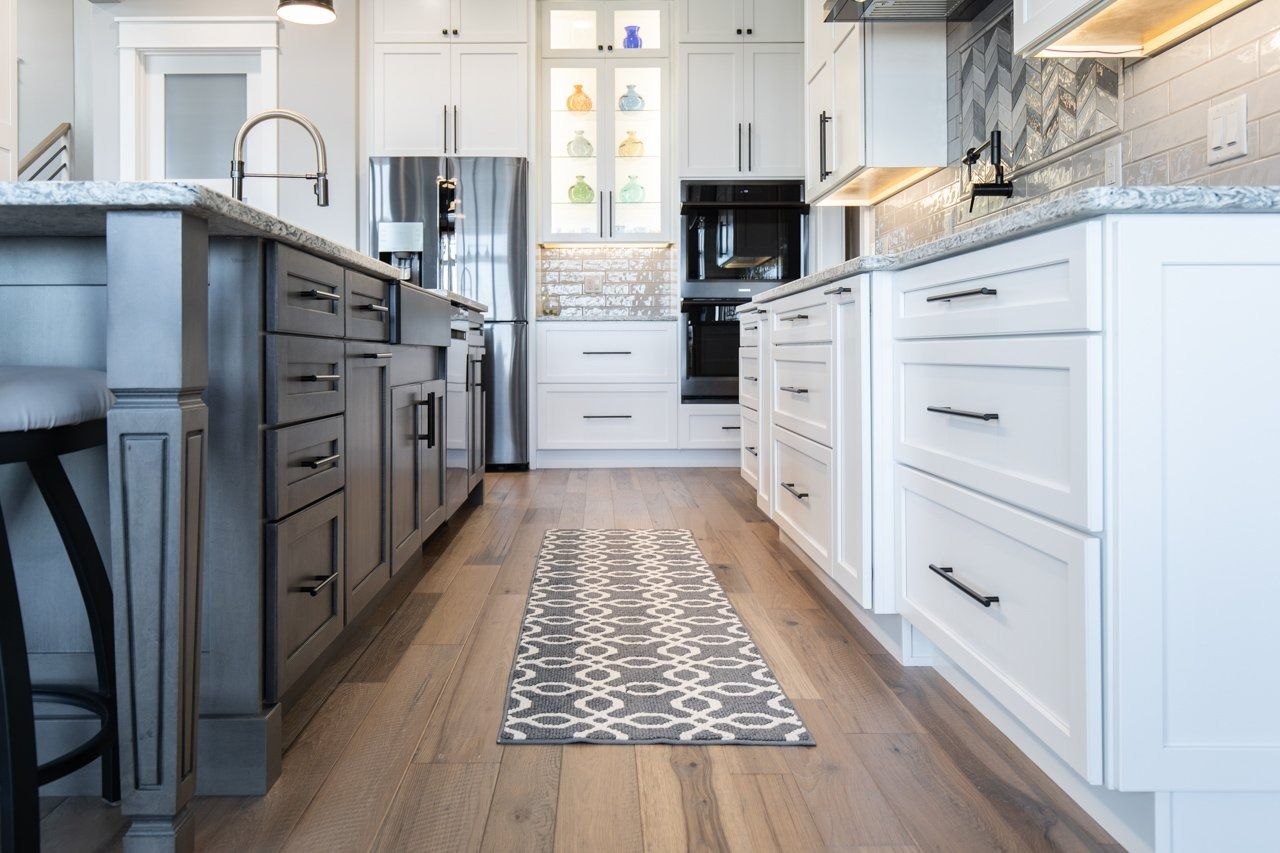 Modern kitchen with white and gray cabinets, stainless steel appliances, and wooden floors.