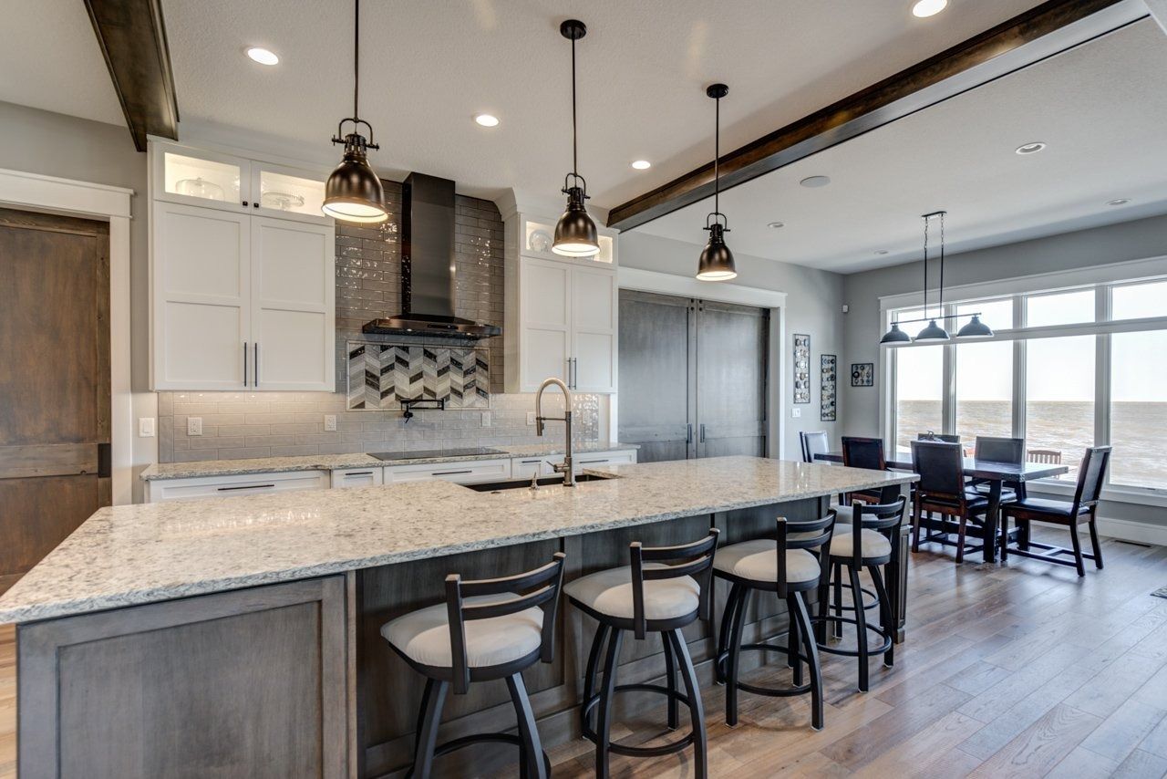 Modern kitchen with island, pendant lights, bar stools, and dining area with large windows.