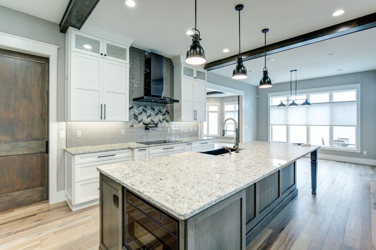 Modern kitchen with white cabinets, gray island, granite countertop, and pendant lights.