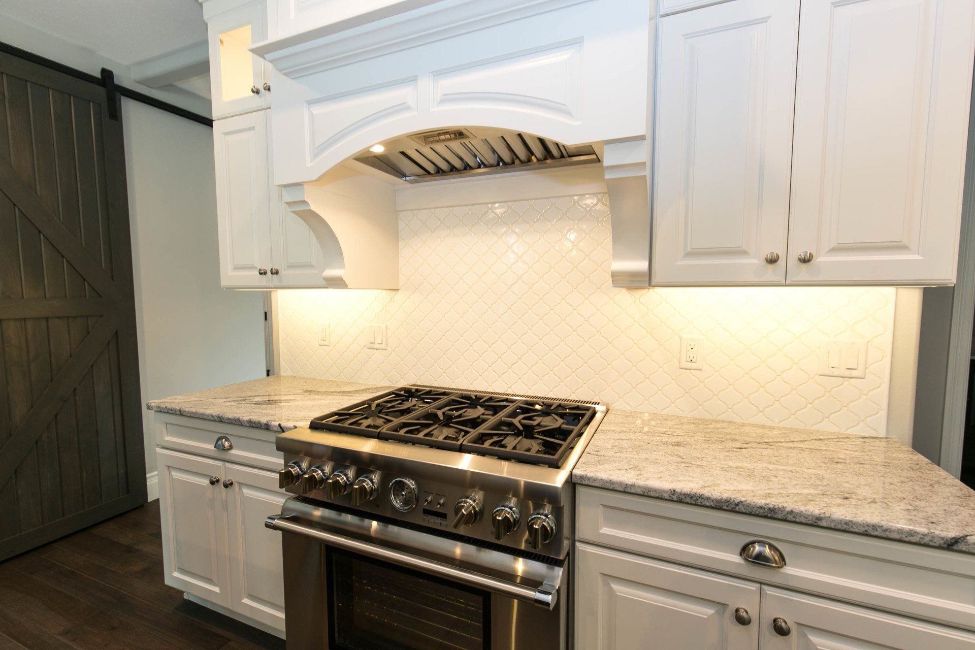 White kitchen cabinets with granite countertops, stainless steel gas range, and range hood.