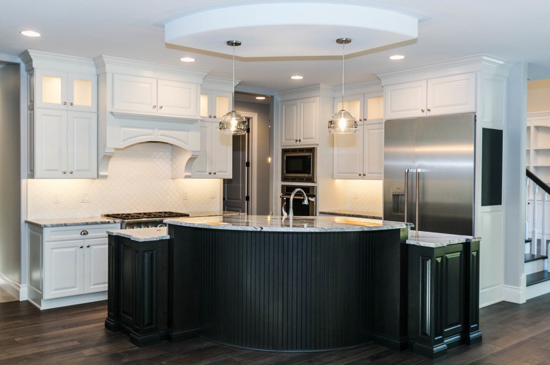 Modern kitchen with white cabinets, dark island, stainless steel appliances, and wood flooring.