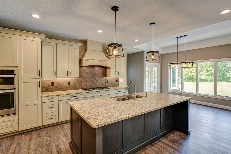 Kitchen with dark island, light cabinets, granite countertops, pendant lights, and large windows.