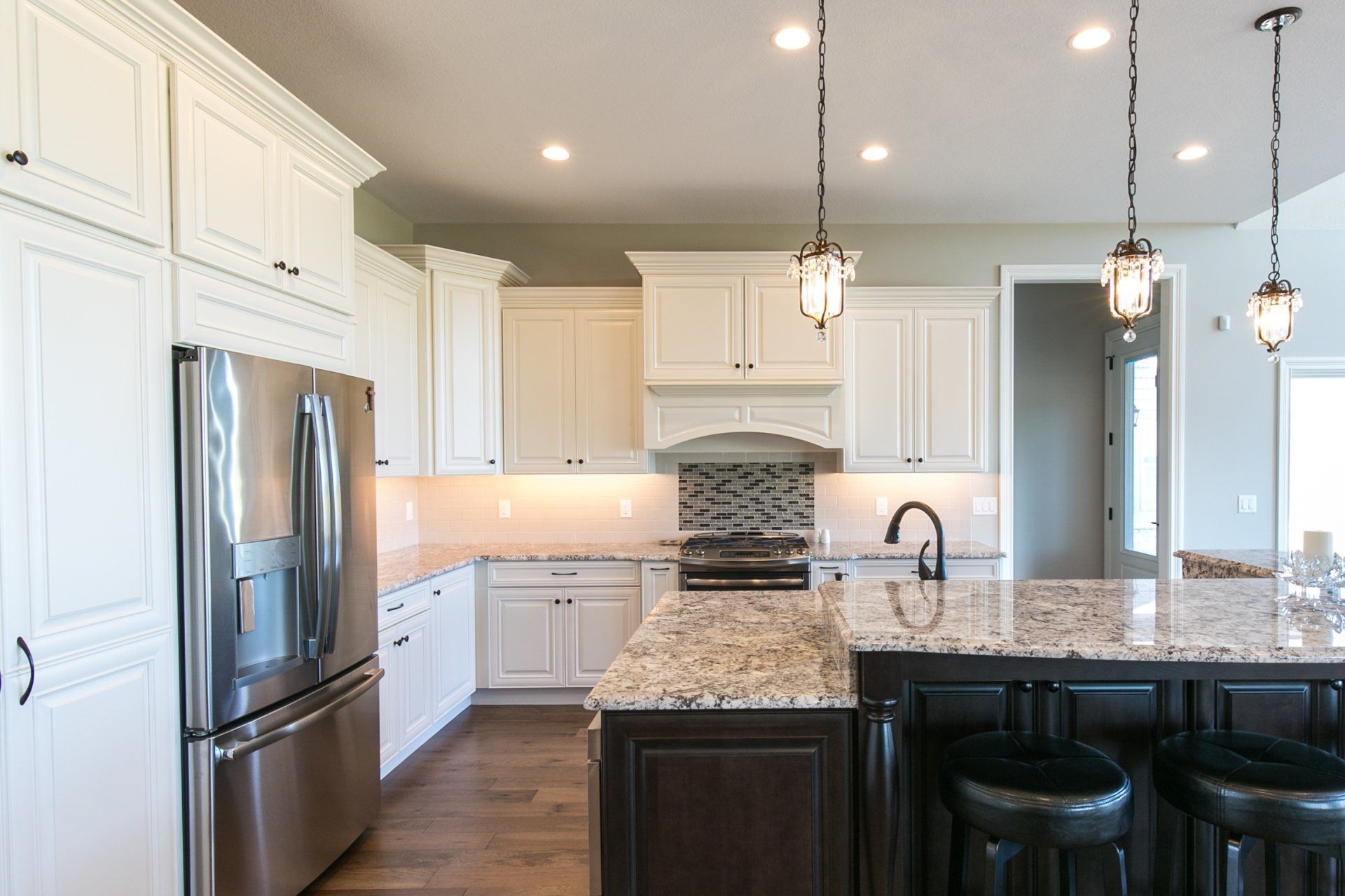 Modern white kitchen with stainless steel appliances, dark island, and pendant lights.