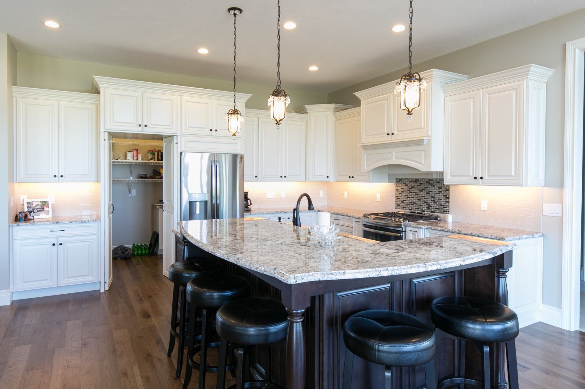 Kitchen with white cabinets, dark island, granite countertop, and pendant lights.