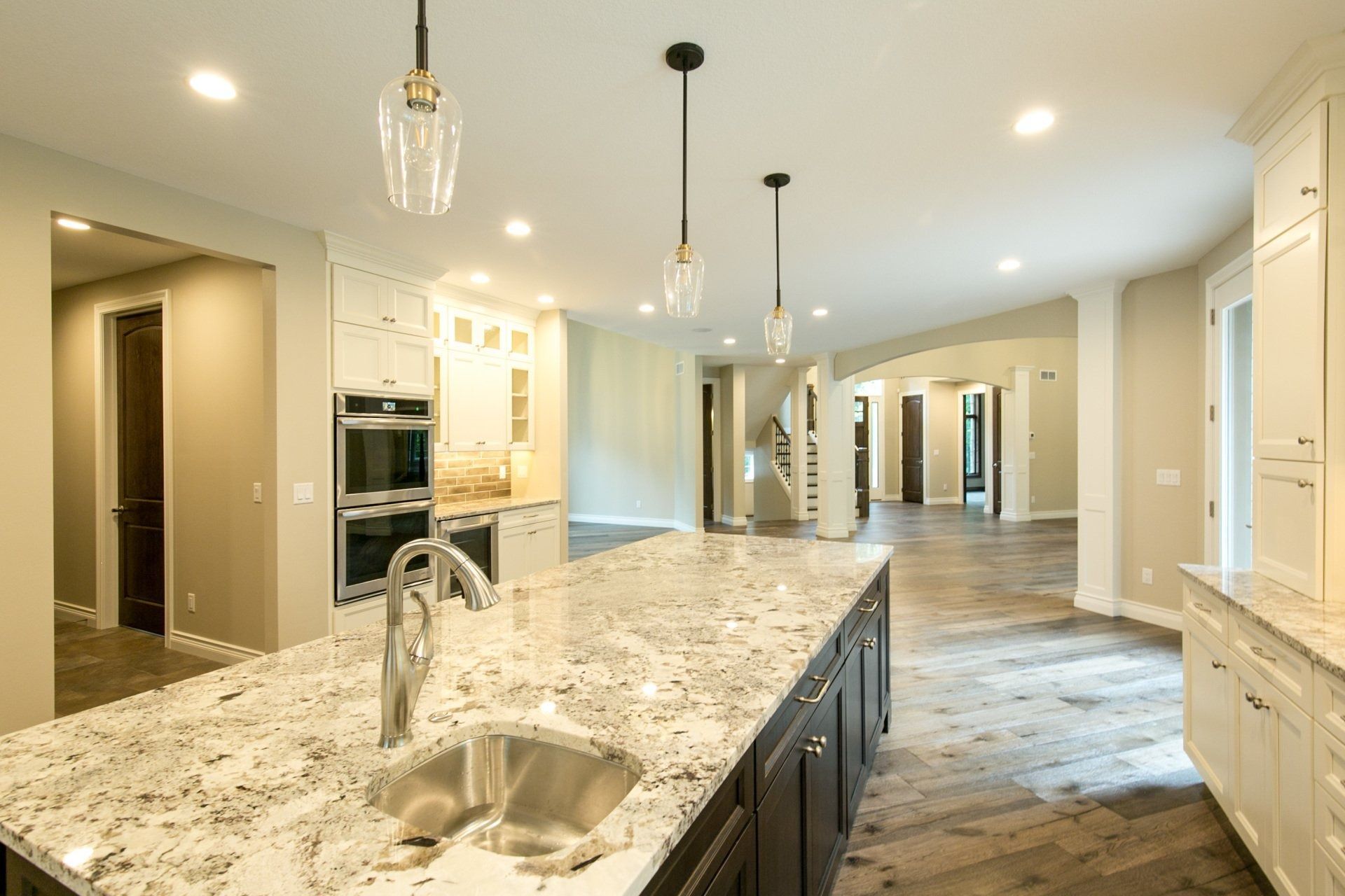 Modern kitchen with a granite island, pendant lights, and wooden floors.