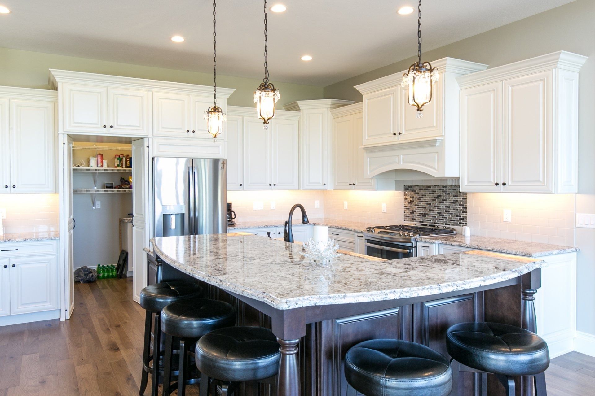 White kitchen with a dark island, granite countertop, pendant lights, and bar stools.