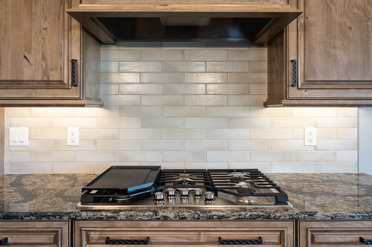 Kitchen with gas stovetop, tile backsplash, wooden cabinets, and granite countertop.