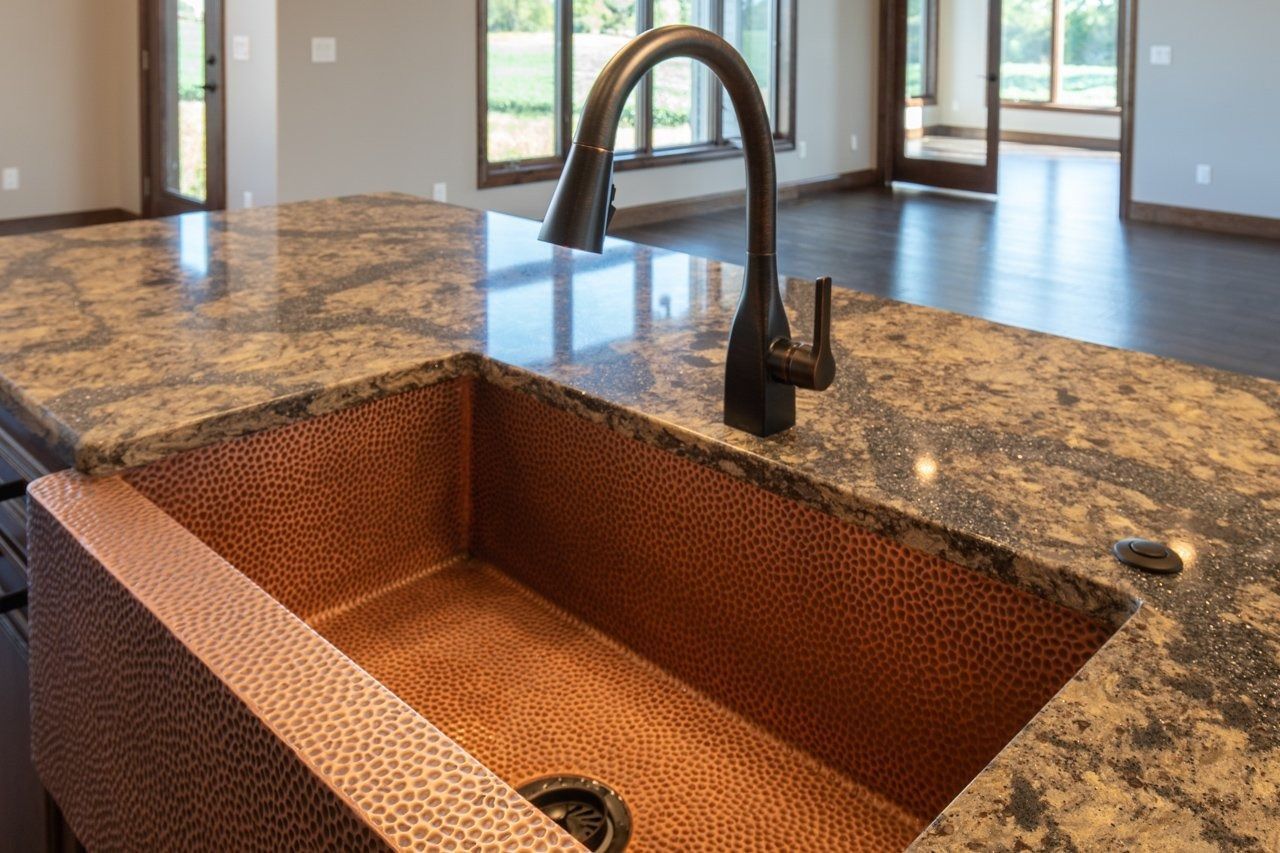 Copper kitchen sink on granite countertop, with dark bronze faucet.