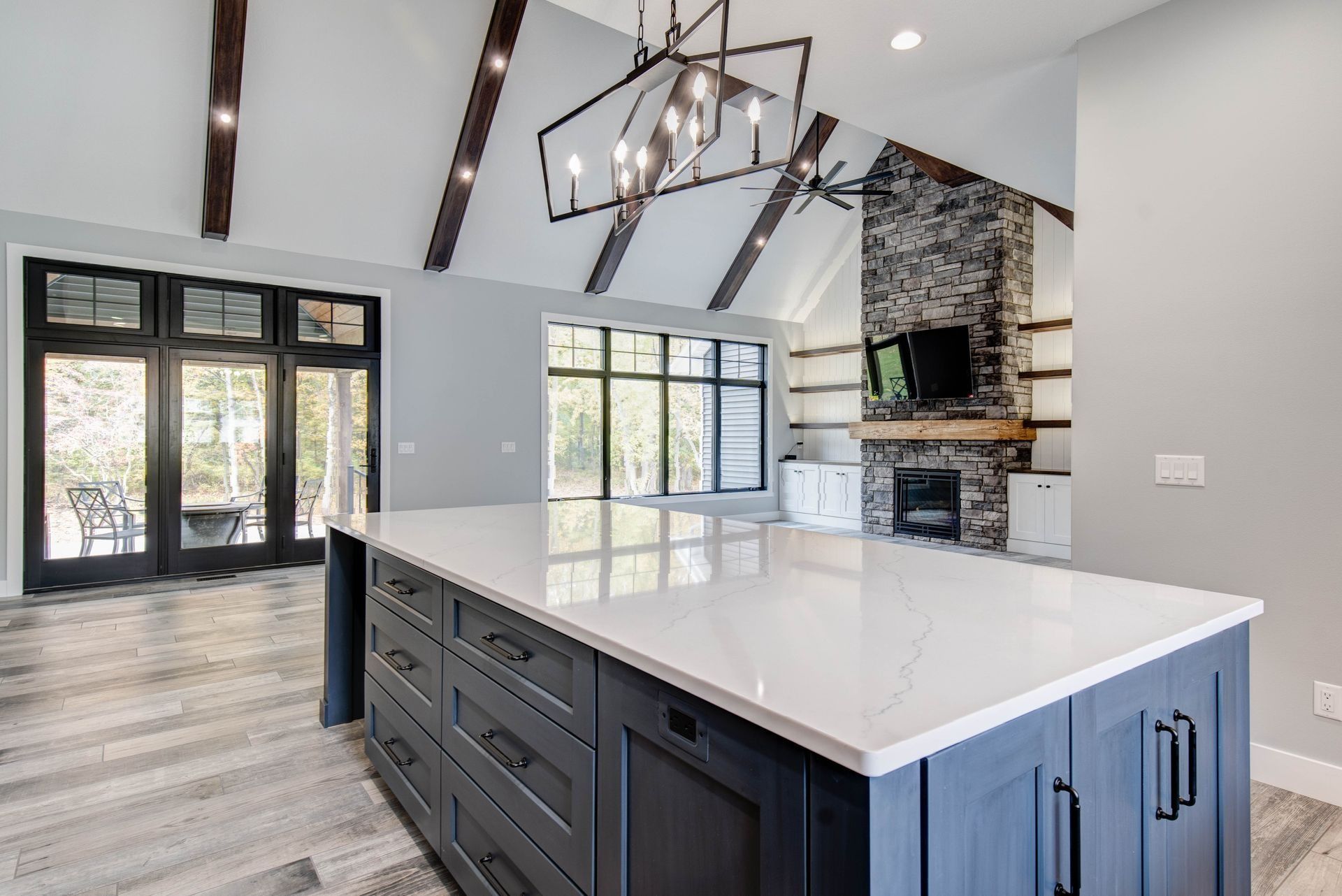Modern kitchen with a large island, dark blue cabinets, and white countertop. Vaulted ceiling, fireplace.