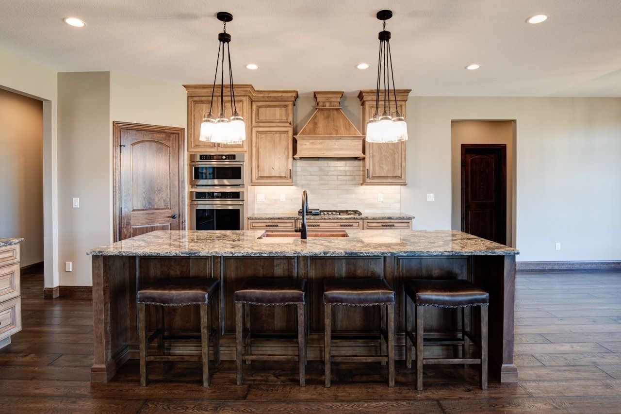 Kitchen with wooden cabinets, island with stools, granite countertops, and pendant lights.