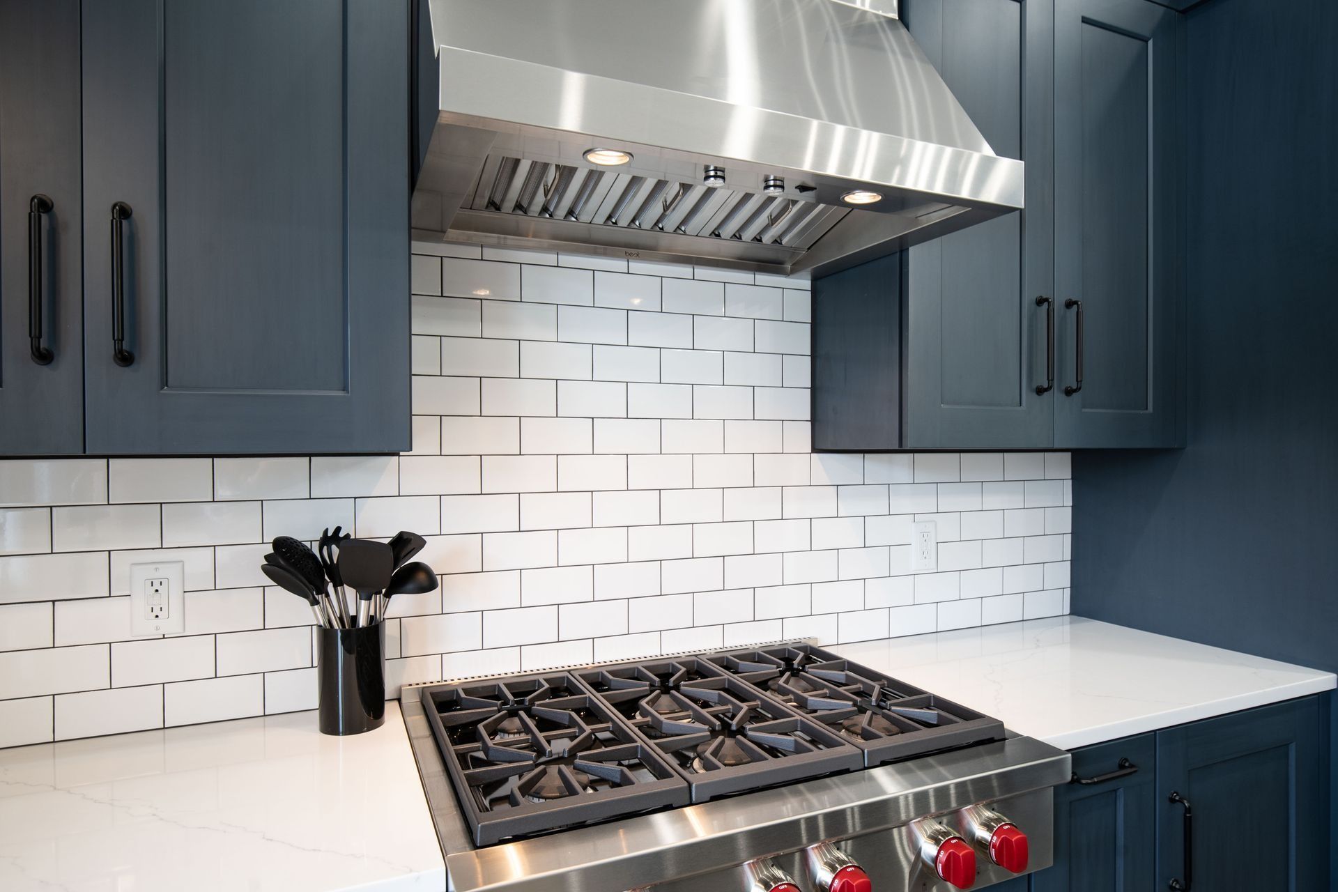 Modern kitchen with blue cabinets, white countertops, stainless steel stove, and white subway tile backsplash.