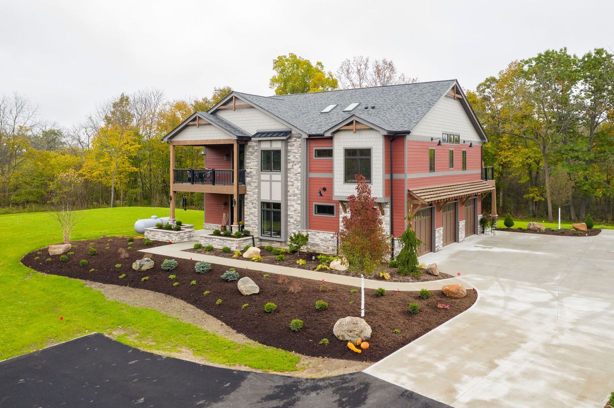 Multi-story house with red siding, stone accents, and a garage, set on landscaped grounds.