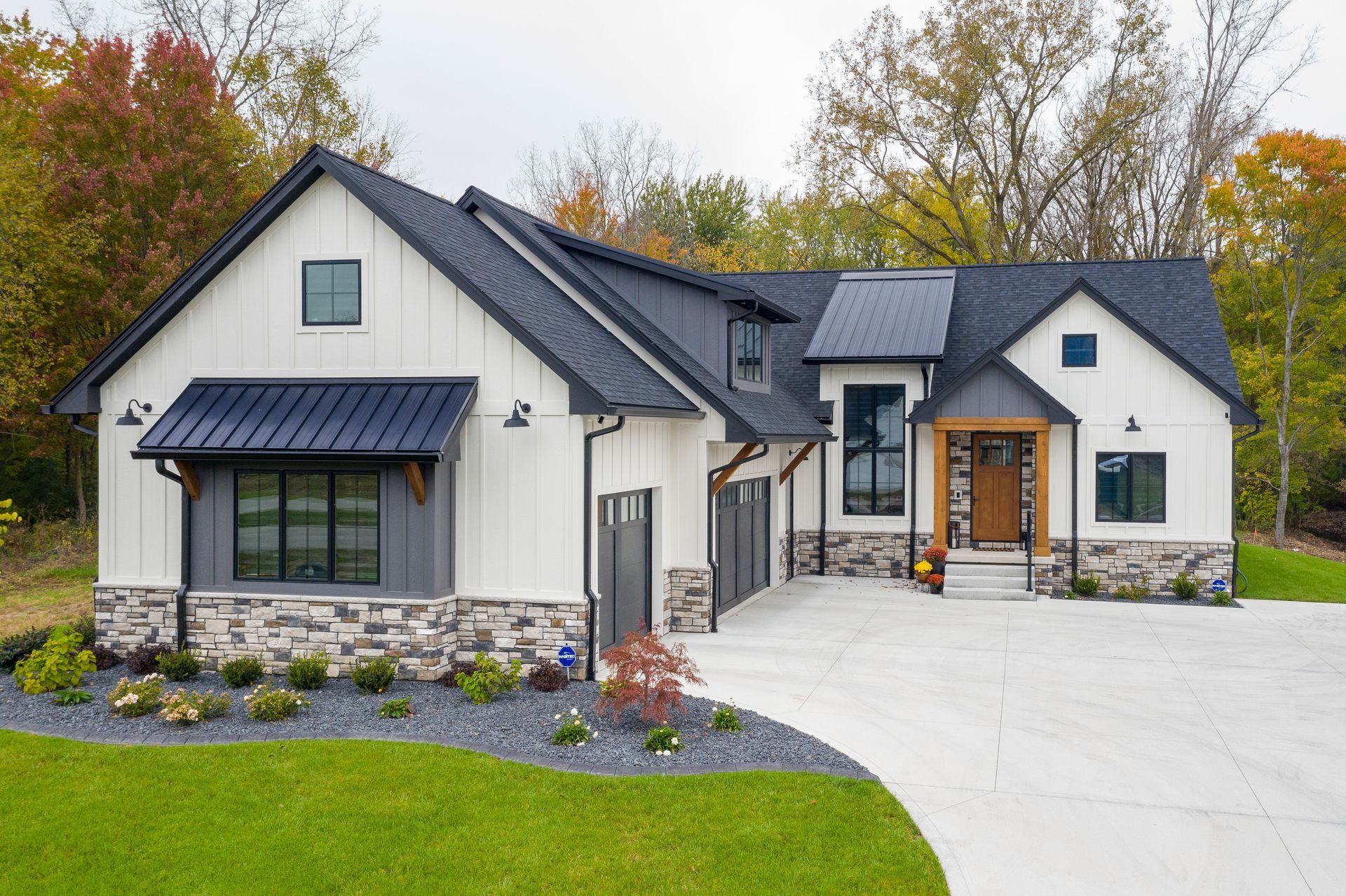 Modern white house with dark gray roof, stone accents, and a concrete driveway.