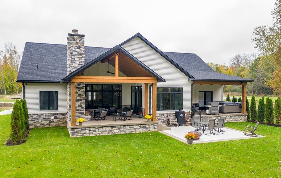 Rear exterior of a white modern home with a covered patio, stone accents, and green lawn.