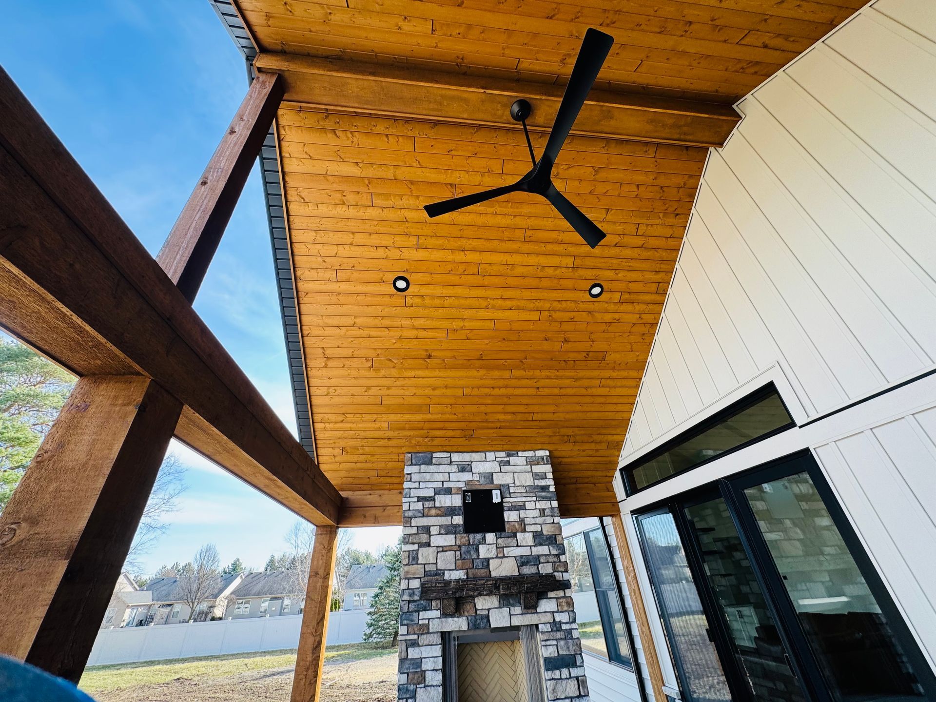 Covered outdoor patio with a fireplace, fan, and wooden ceiling.