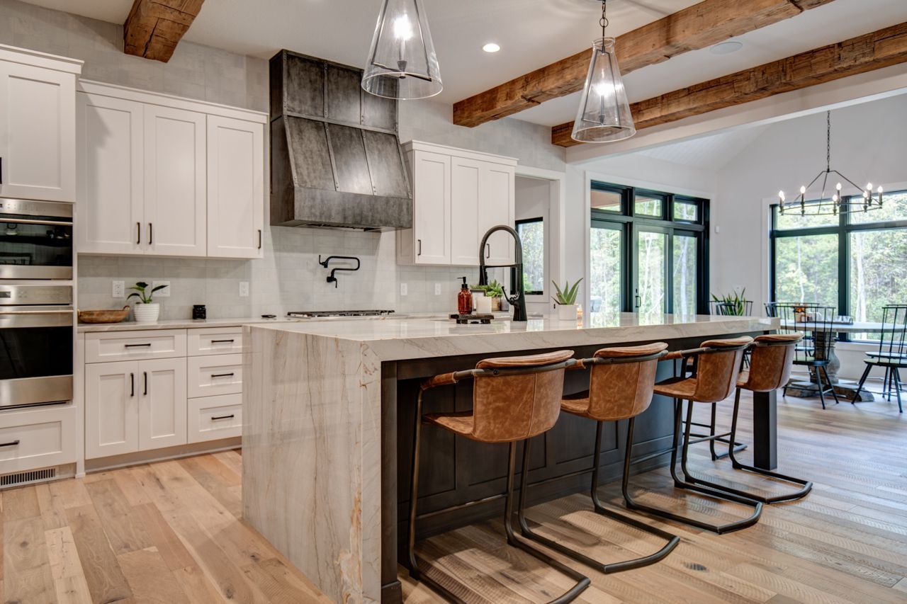 Modern kitchen with white cabinets, wood island with brown bar stools, and wooden beams.