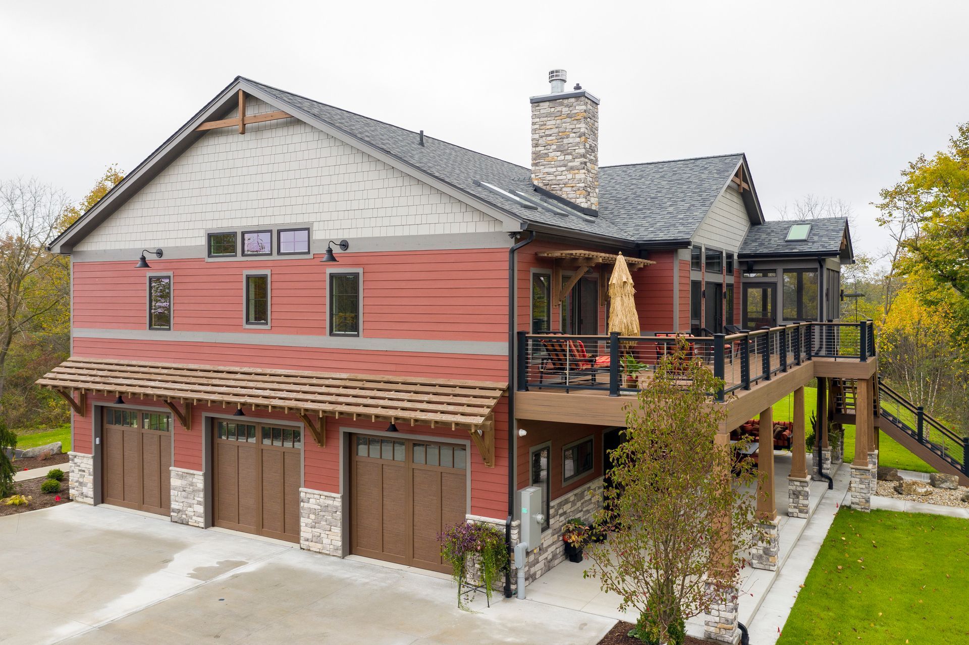 Multi-story home with red and gray siding, three-car garage, and deck overlooking a green lawn.