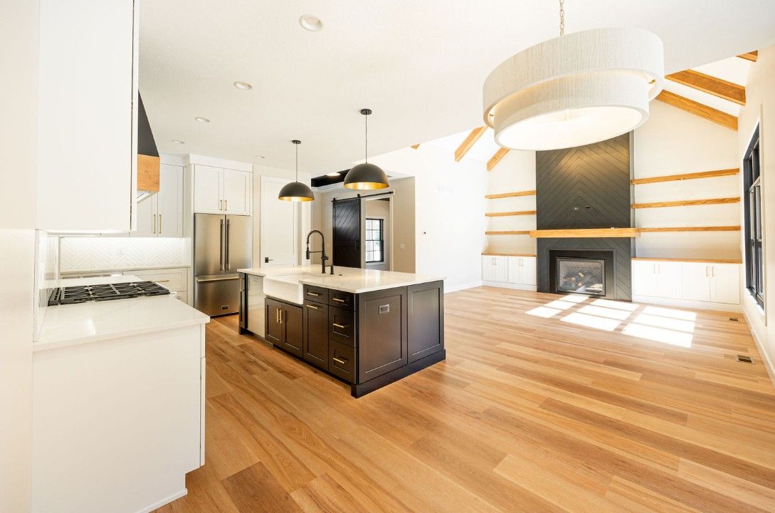 Spacious kitchen with wood floors, island, and fireplace with open shelving and large light fixture.