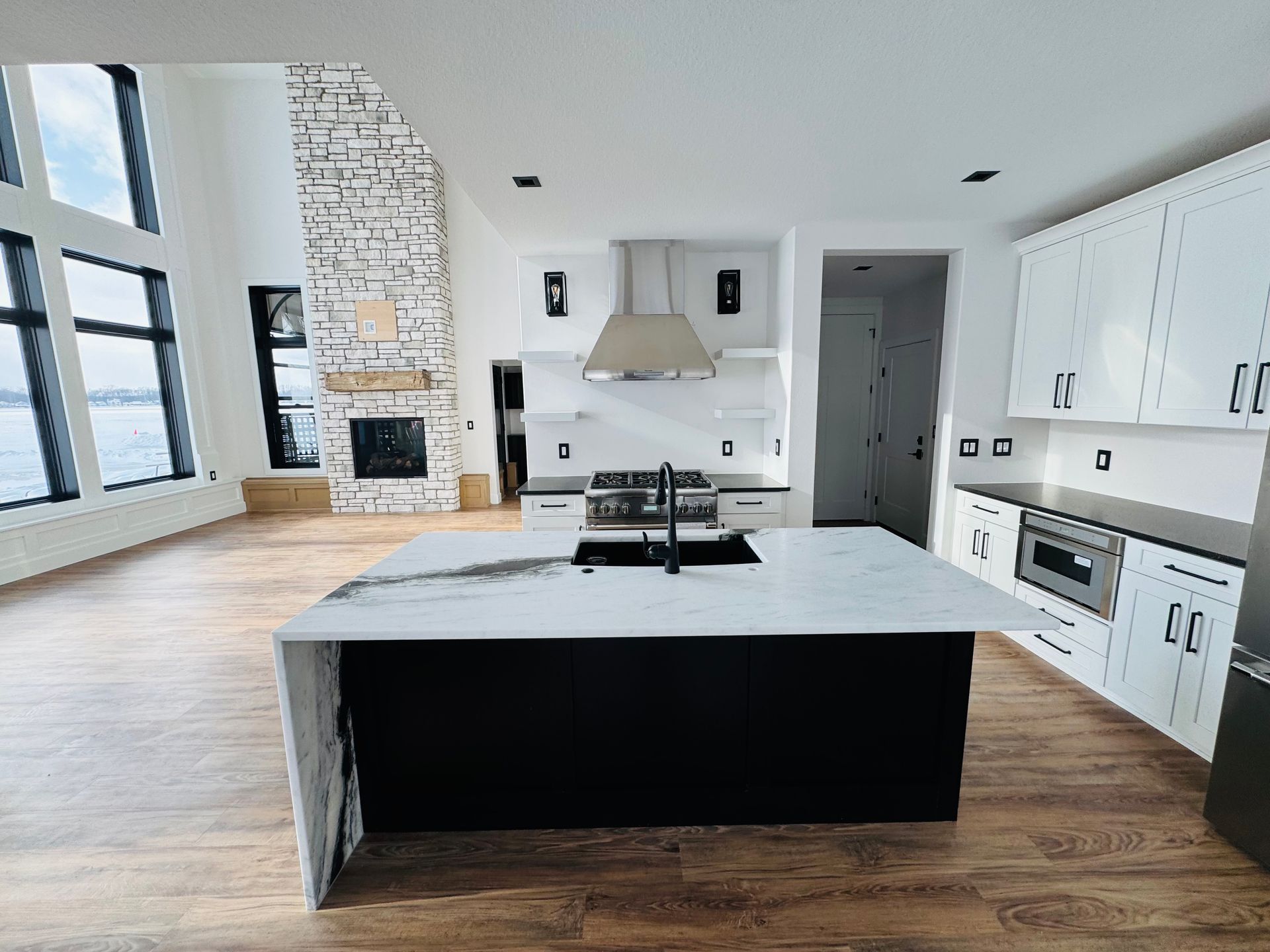 Modern kitchen with black island, white countertops, stainless steel appliances, and a stone fireplace.
