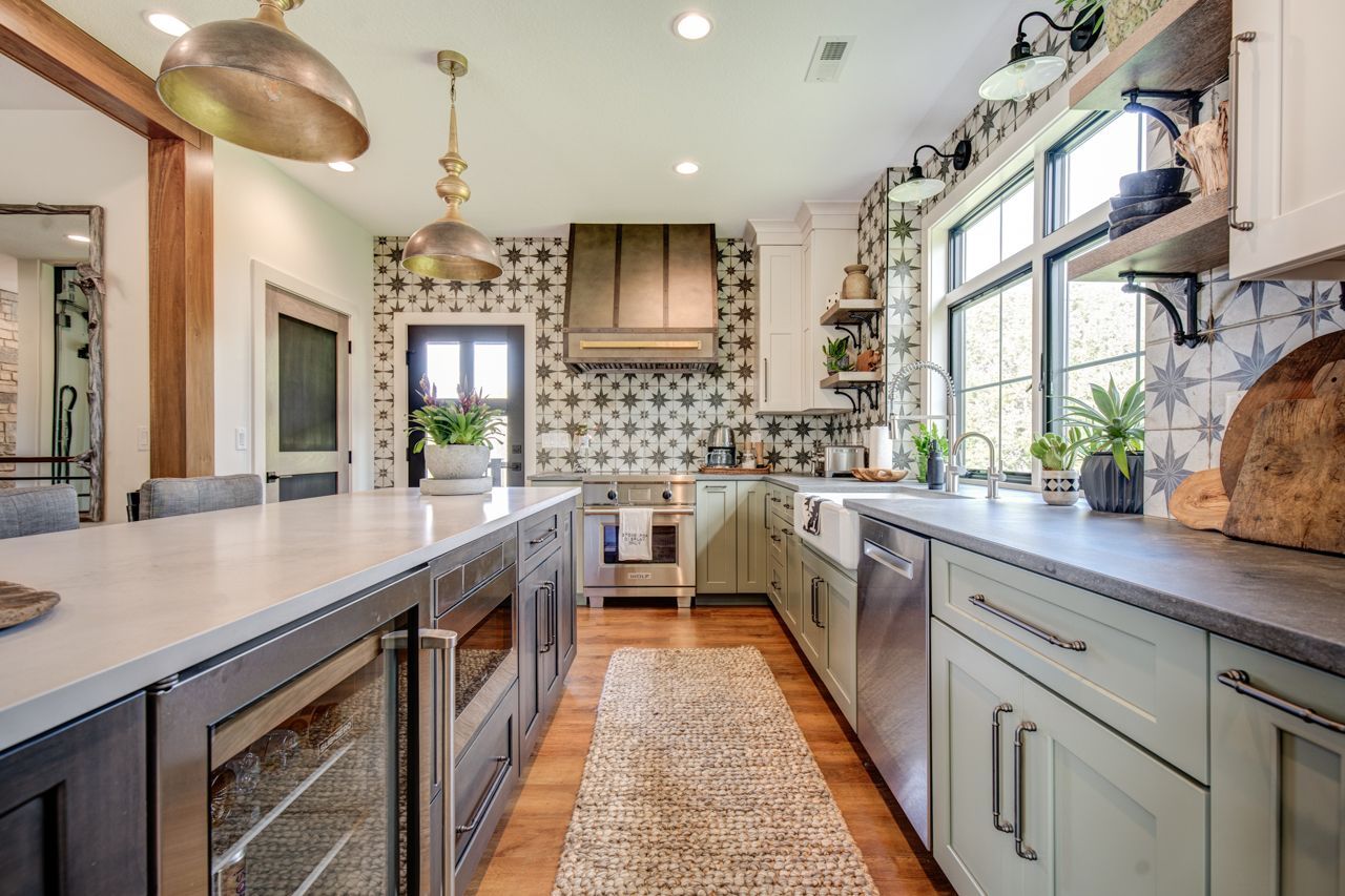 Spacious kitchen with island and sink, light green cabinets, patterned backsplash, and gold light fixtures.