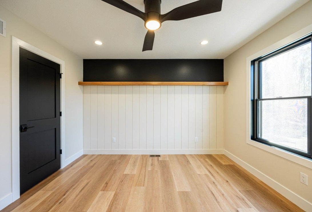 Empty room with wood floors, black door, and accent wall with shelf, recessed lighting.