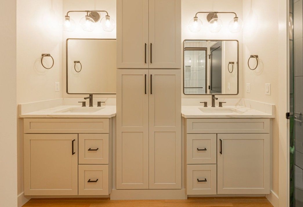 Bathroom with two vanities, white cabinets, mirrors, and a central storage unit.