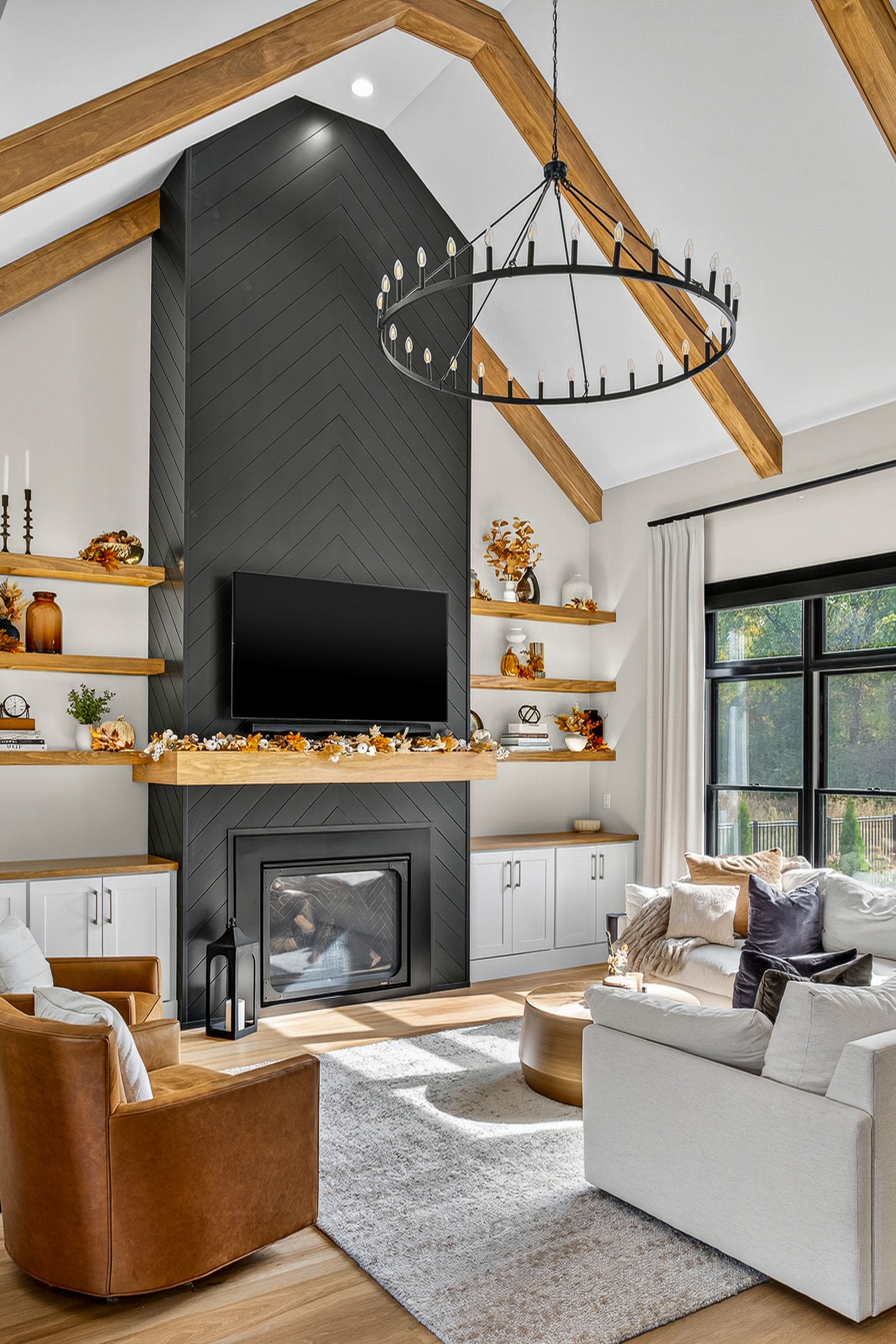 Living room with fireplace, TV, and shelves. Neutral tones with a chandelier and exposed beams.