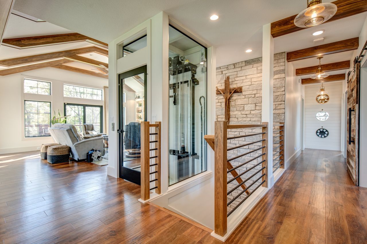 Hallway with wooden beams, brick accent wall, stairs, and a glass-enclosed elevator.