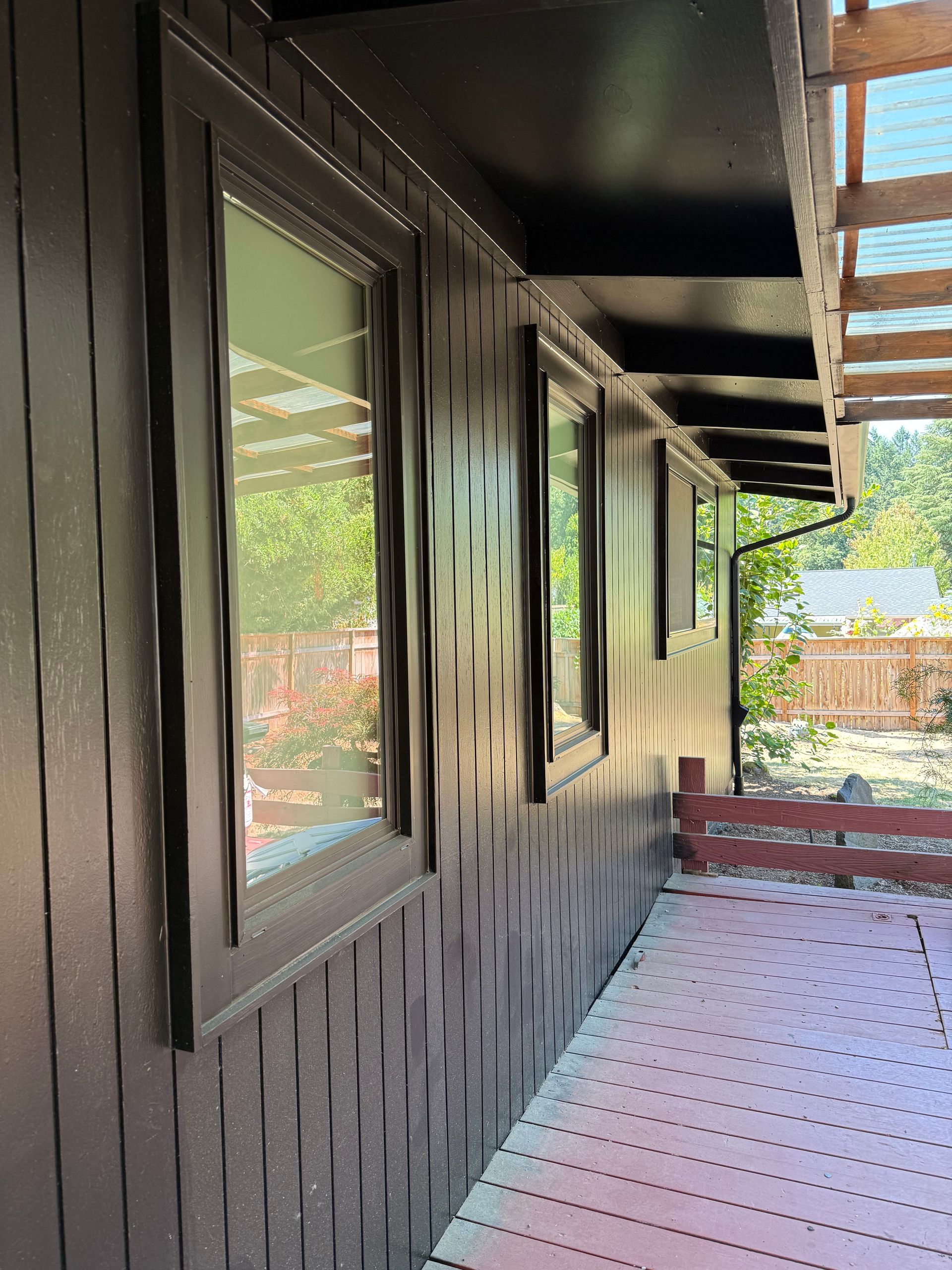 Dark brown exterior wall with windows, deck, and pergola, in natural light.