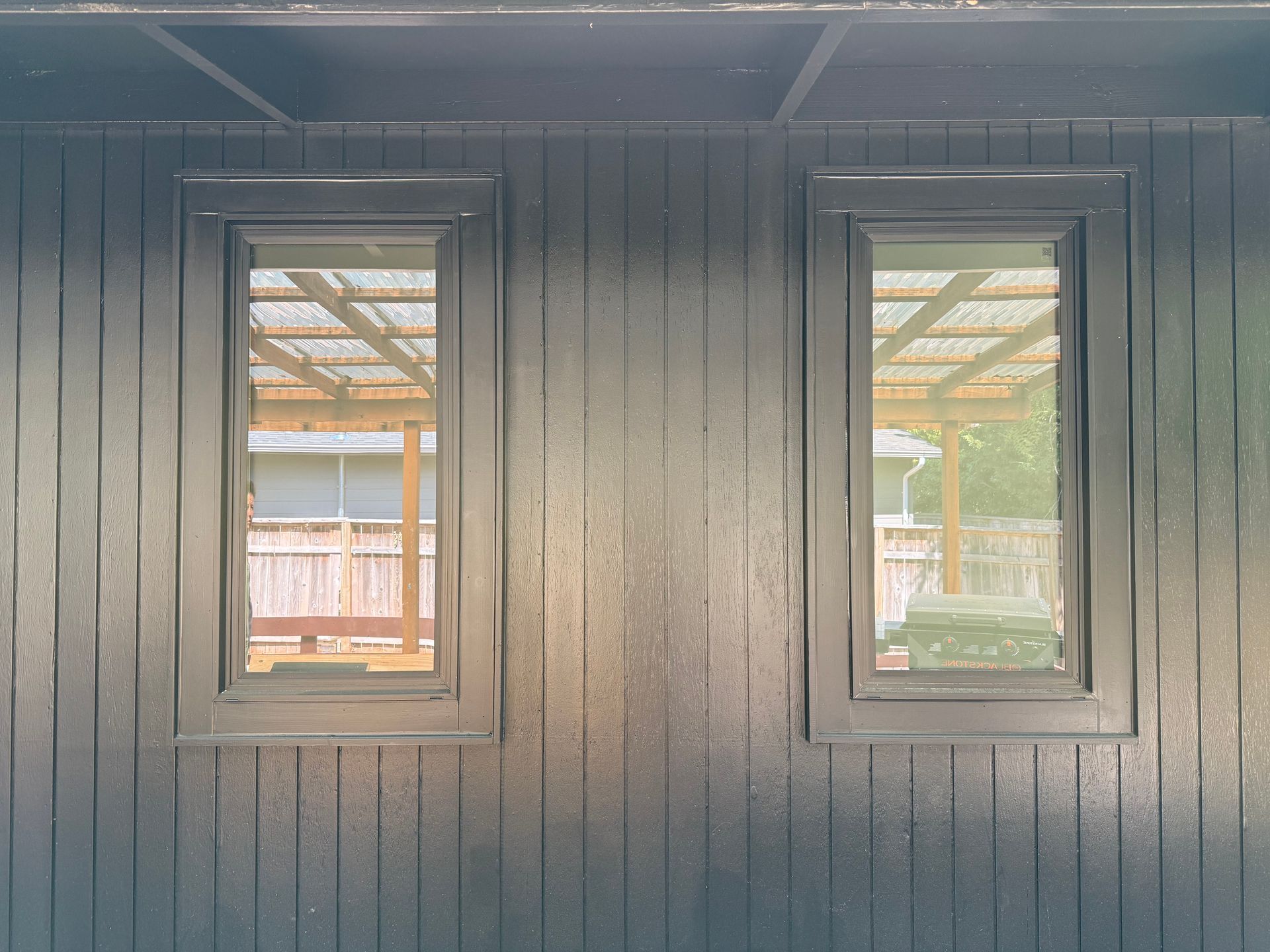Two black-framed windows on a black painted wall reflect an outdoor patio setting.