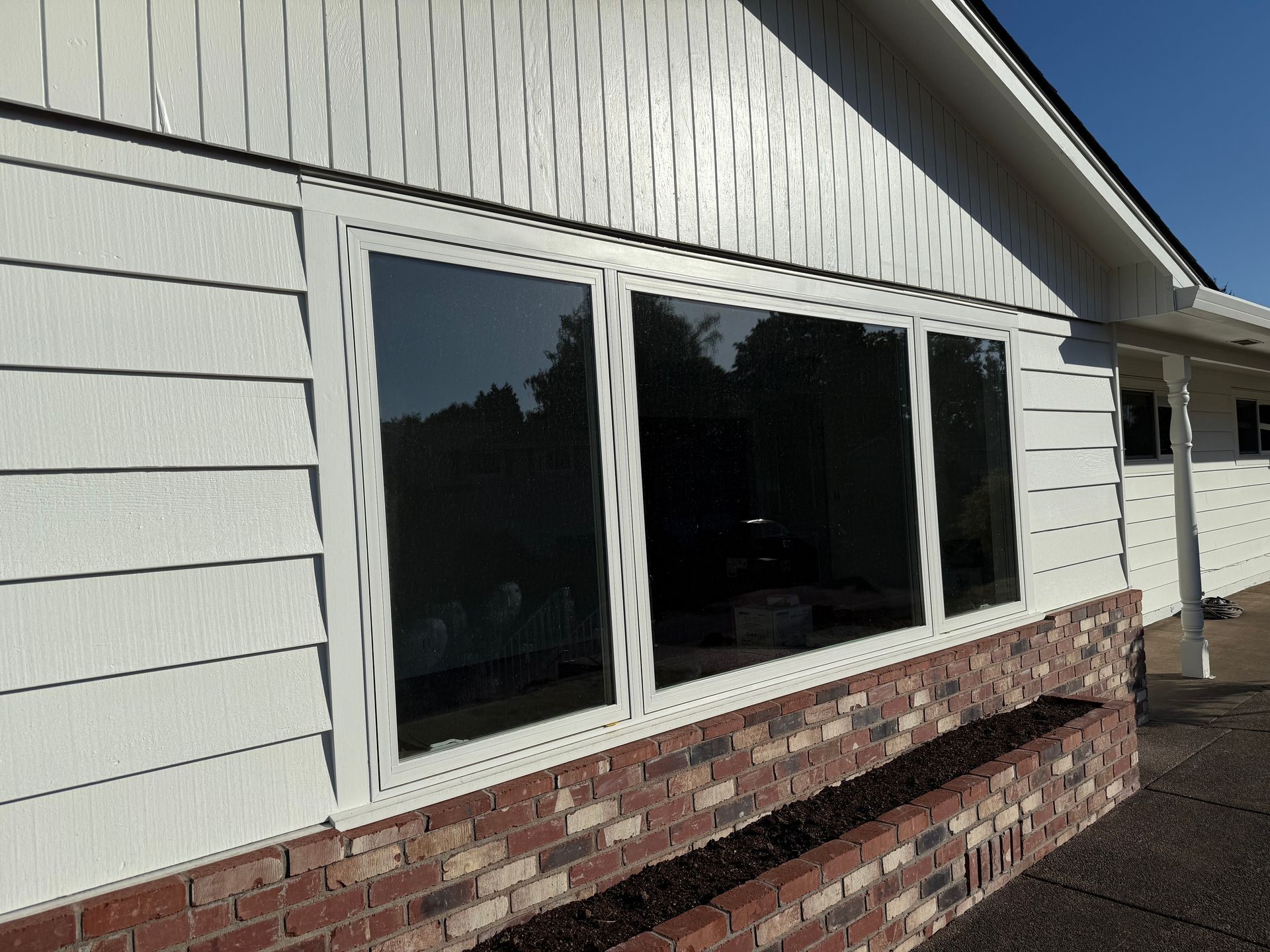 White house exterior with three large windows over a brick planter; white siding and blue sky.