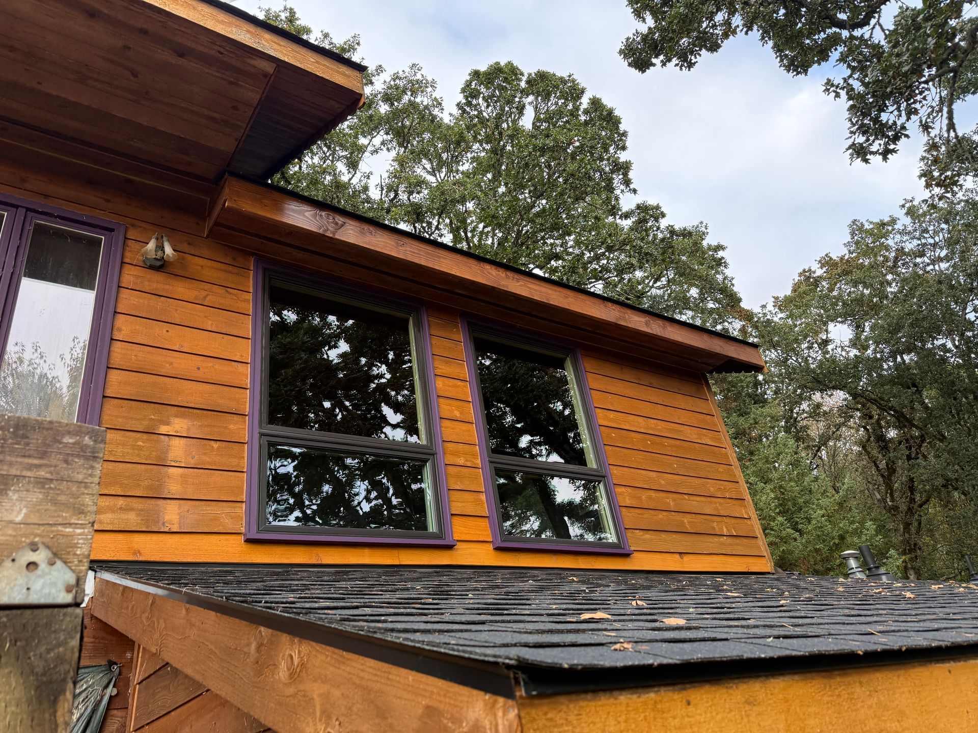 Orange-sided building with two windows and angled roof, set against a backdrop of trees and a cloudy sky.