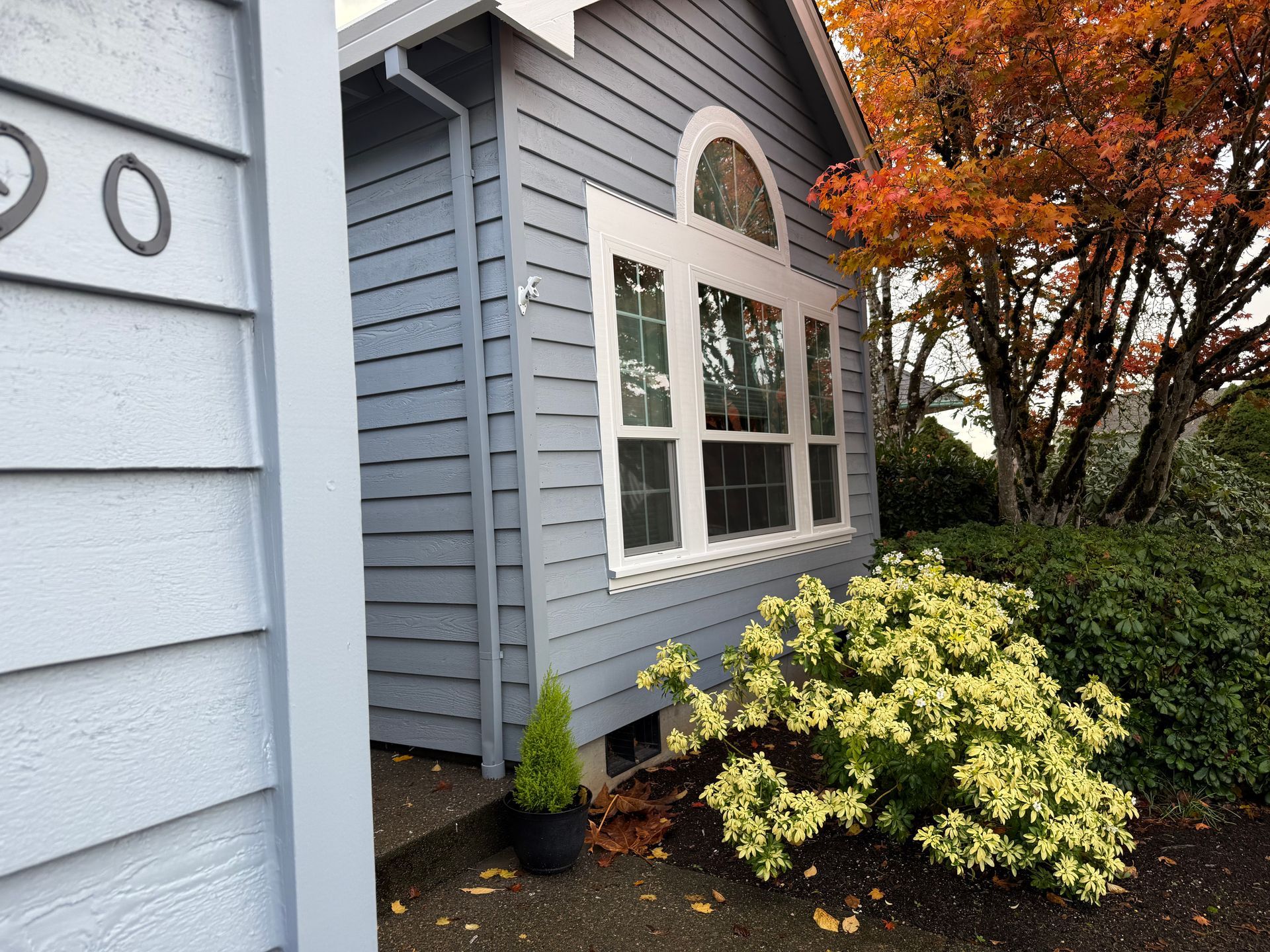 Blue house with white trim, arched window, and fall foliage.