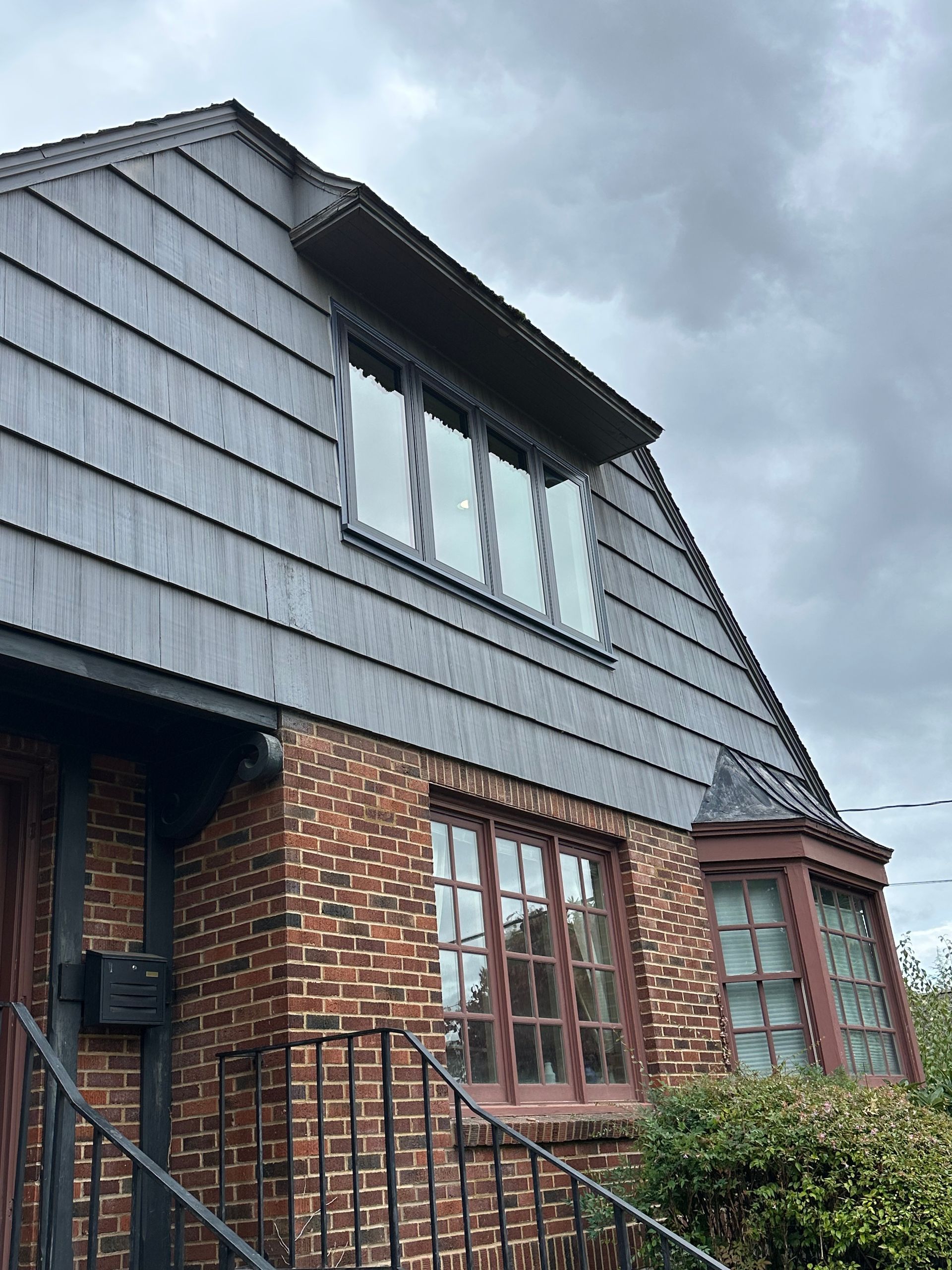 Brick house with gray shingle roof, arched window, and bay window under a cloudy sky.