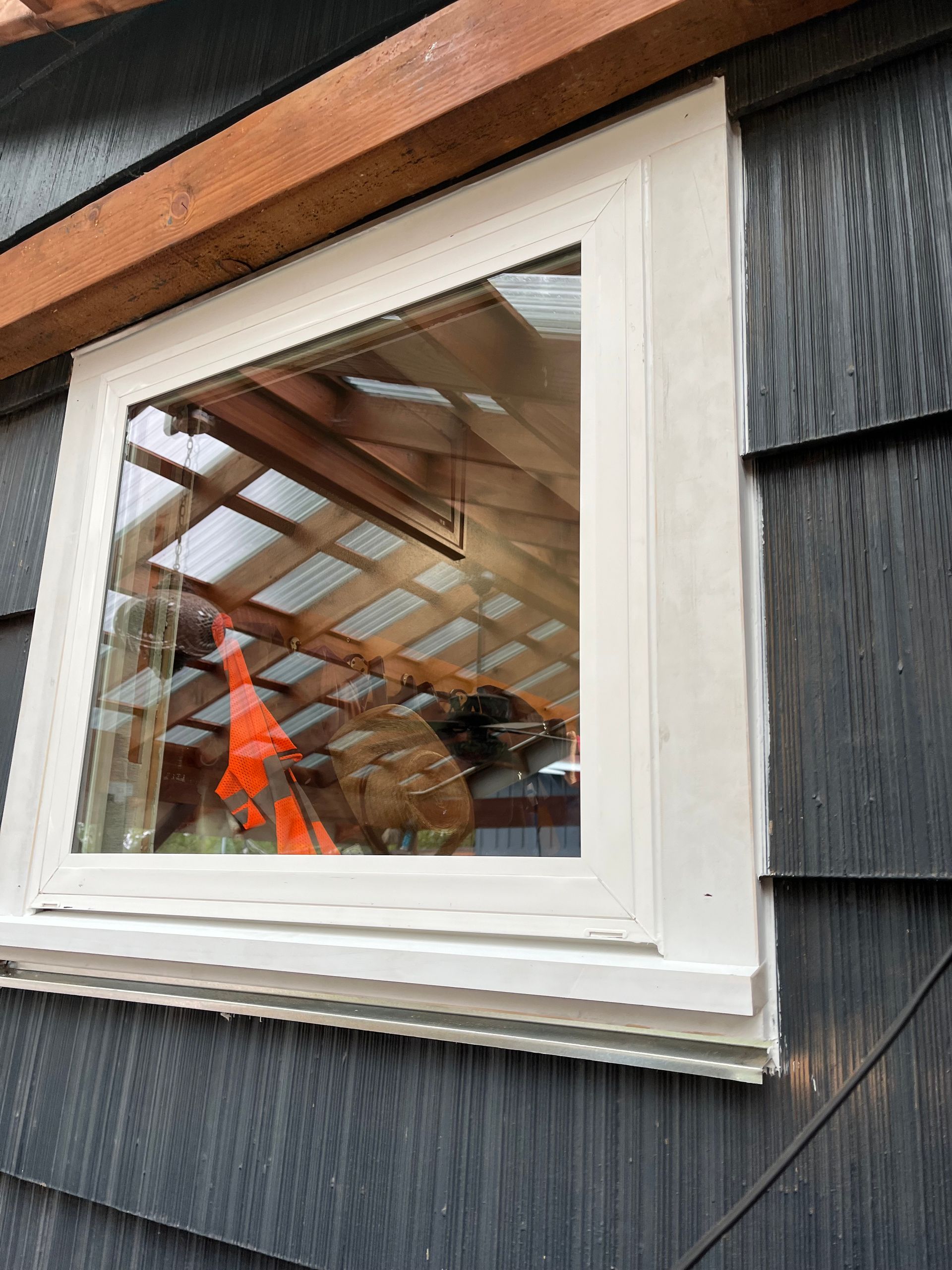 Yellow level resting on a windowsill, measuring the window's alignment. Window frame, house visible through the glass.
