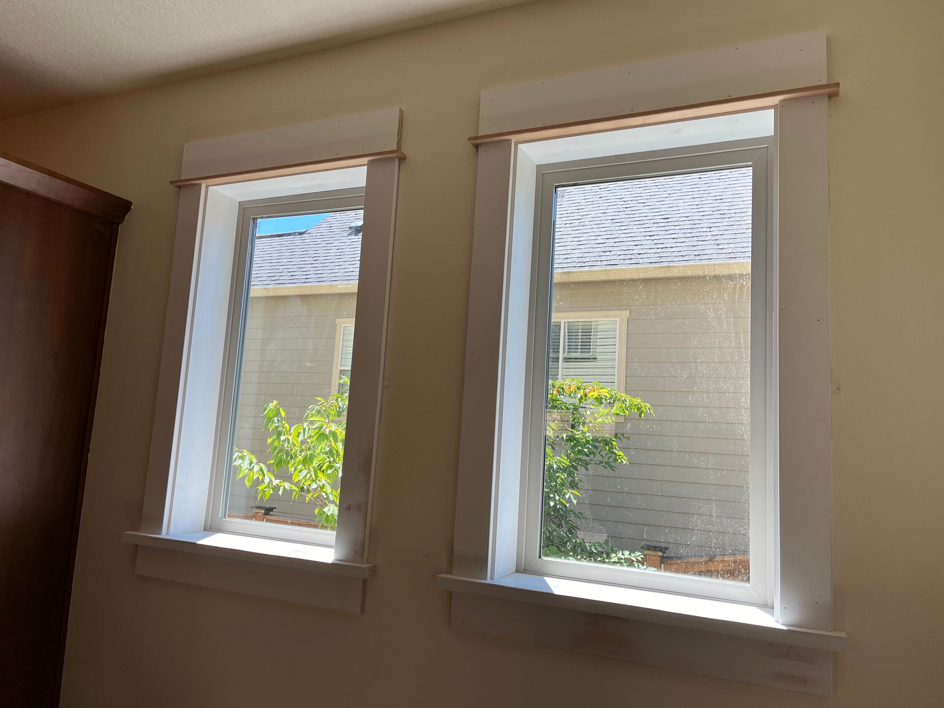 Two white-framed windows with decorative top and bottom trim. Outside view includes green shrubbery and a white building.