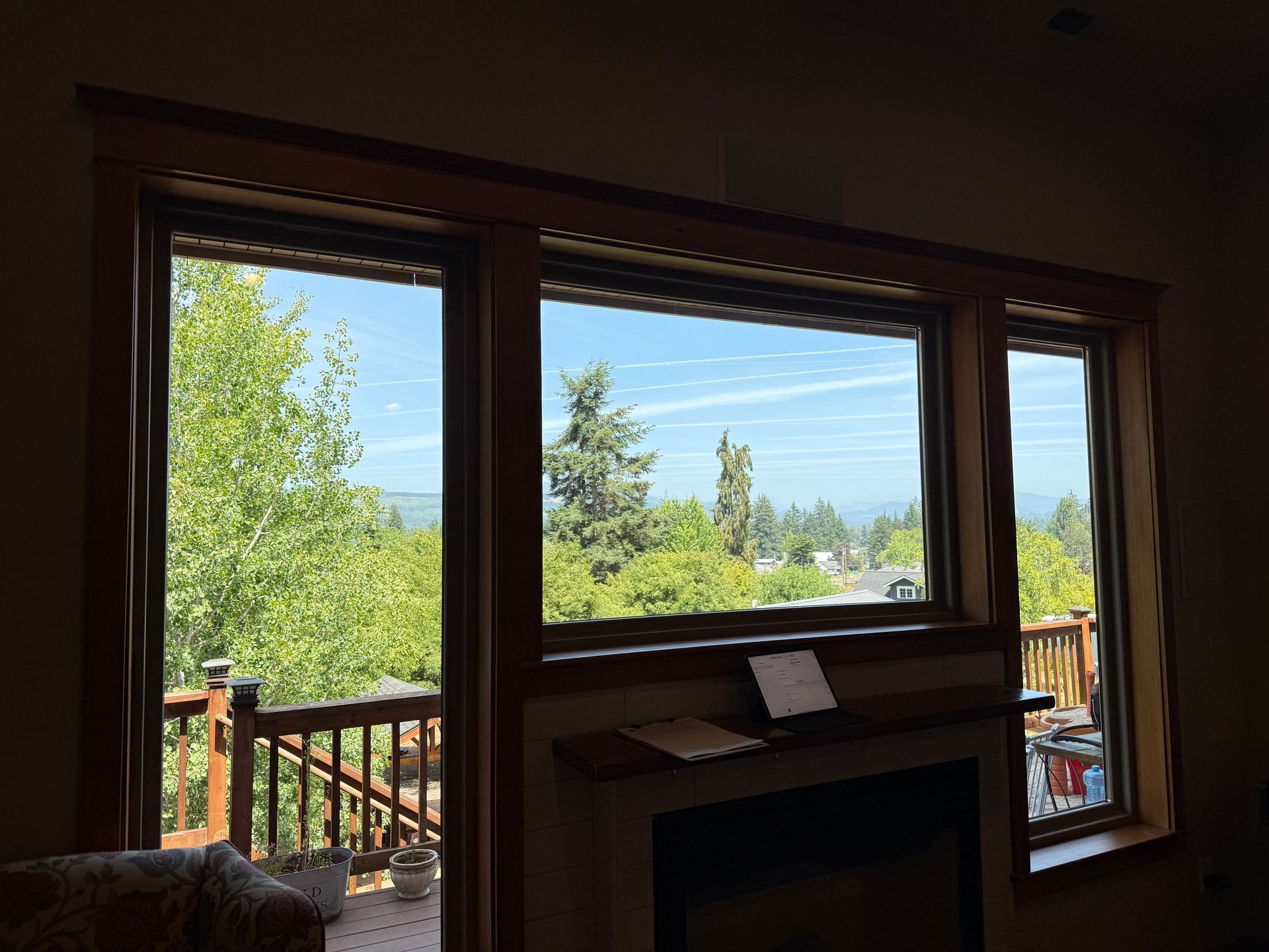 Three windows with a view of trees and sky framed by brown wood trim, and a fireplace below.