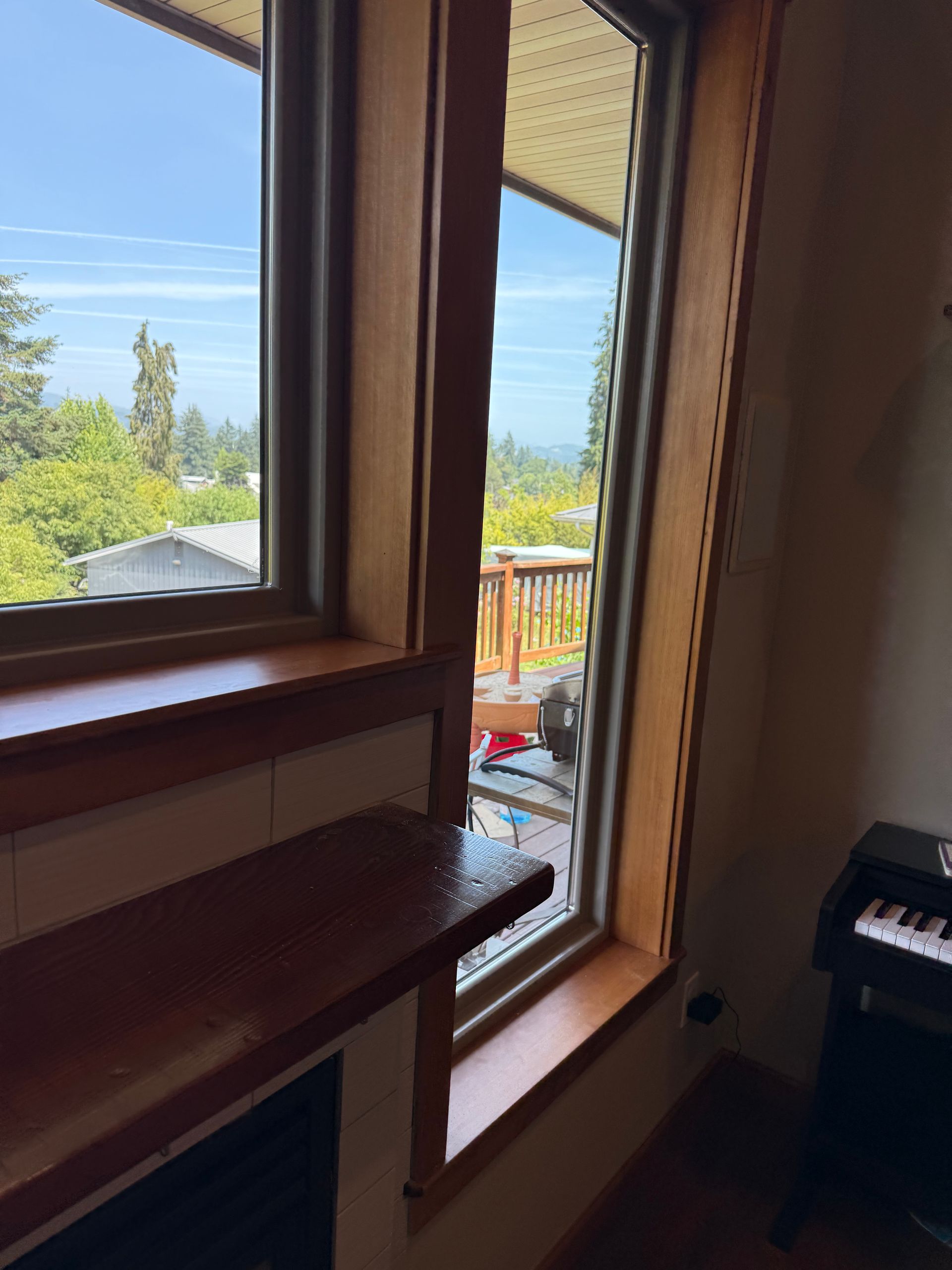Wooden-framed windows with a view of trees and a deck, interior shot. A small keyboard is in the corner.